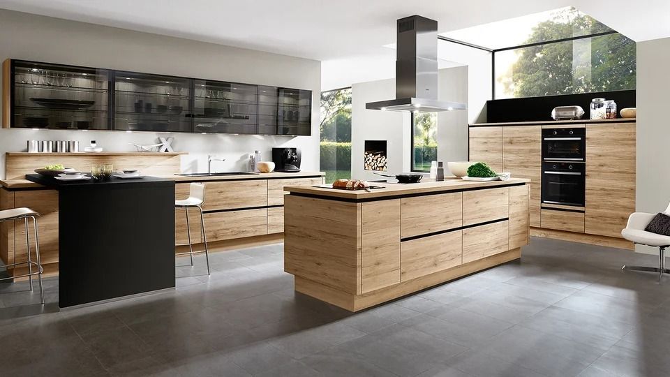 Cucina moderna con mobili in legno, dettagli neri, isola centrale e ampie finestre con vista sul verde.