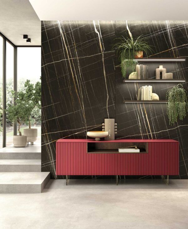 Soggiorno moderno con consolle rossa, parete in marmo scuro, mensole, piante e scala che conduce al patio.