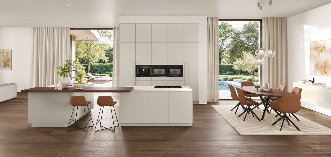 Cucina e zona pranzo luminose e moderne con mobili bianchi, pavimenti in legno e ampie finestre che si affacciano sul verde.