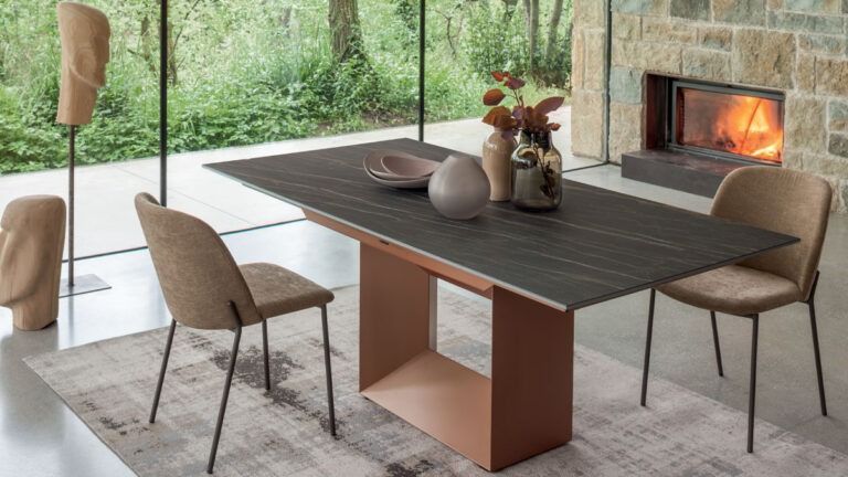 Sala da pranzo moderna con tavolo in legno scuro, sedie color cuoio, tappeto e camino acceso accanto a grandi finestre.
