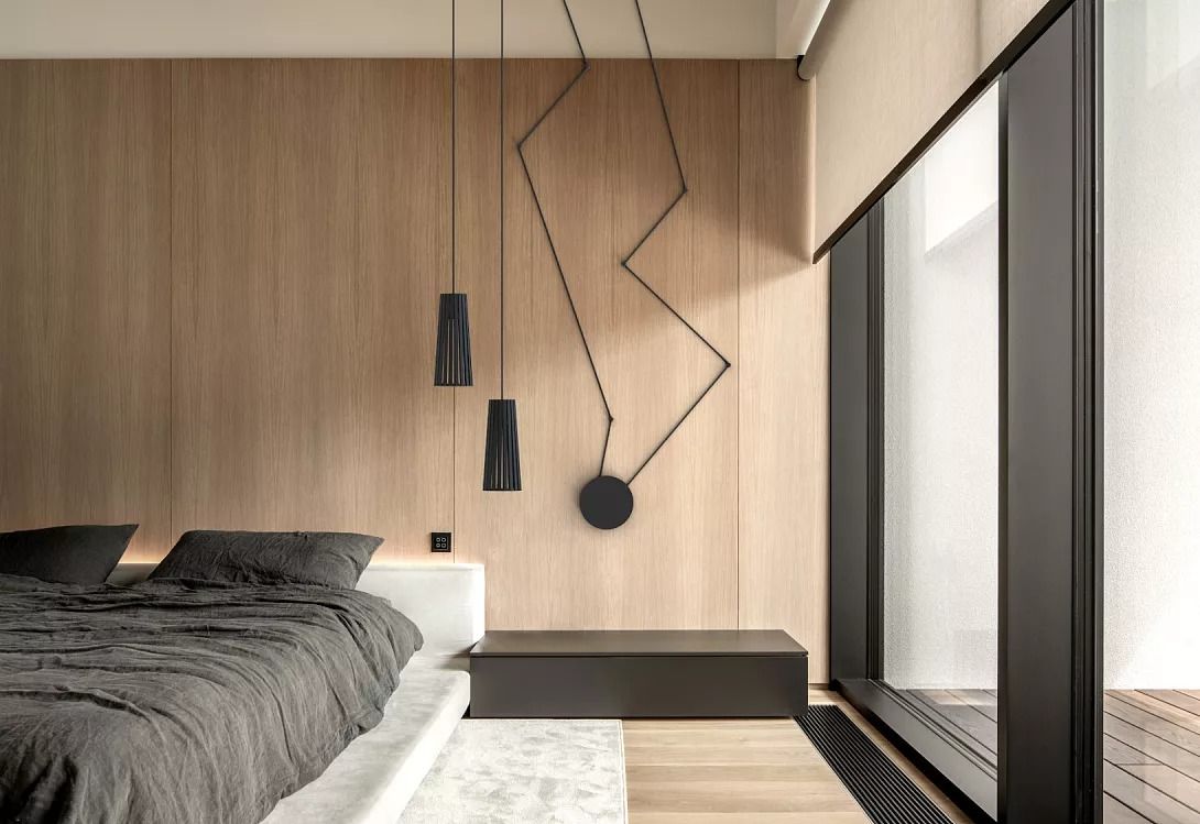 Camera da letto moderna e minimalista con parete rivestita in legno, lampade a sospensione nere e ampie finestre a tutta altezza.