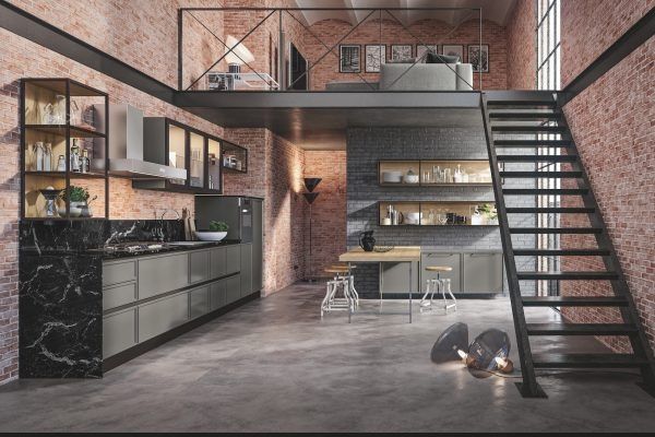 Cucina moderna in stile loft con scala nera, pareti in mattoni, soppalco e pavimento in cemento grigio.