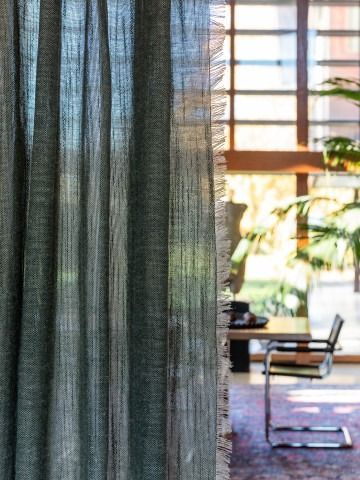Tenda trasparente accanto a un ufficio illuminato dal sole con scrivania, sedia e piante.