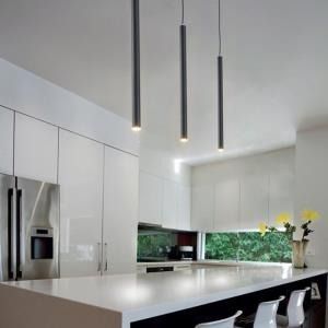 Cucina moderna bianca con isola in marmo, frigorifero in acciaio inox e tre lampade a sospensione nere.