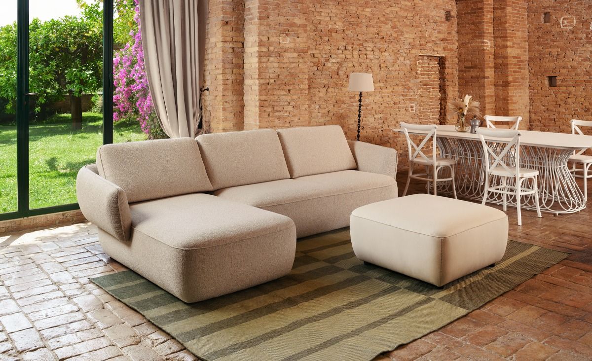 Patio moderno con divano componibile beige e pouf accanto a un muro di mattoni e set da pranzo bianco per esterni.