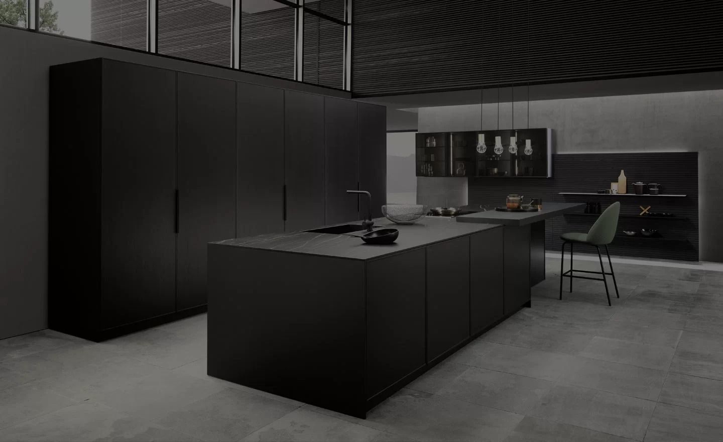 Cucina moderna nera con isola, eleganti mobili, sgabelli da bar e pavimento in cemento in uno spazio industriale poco illuminato.
