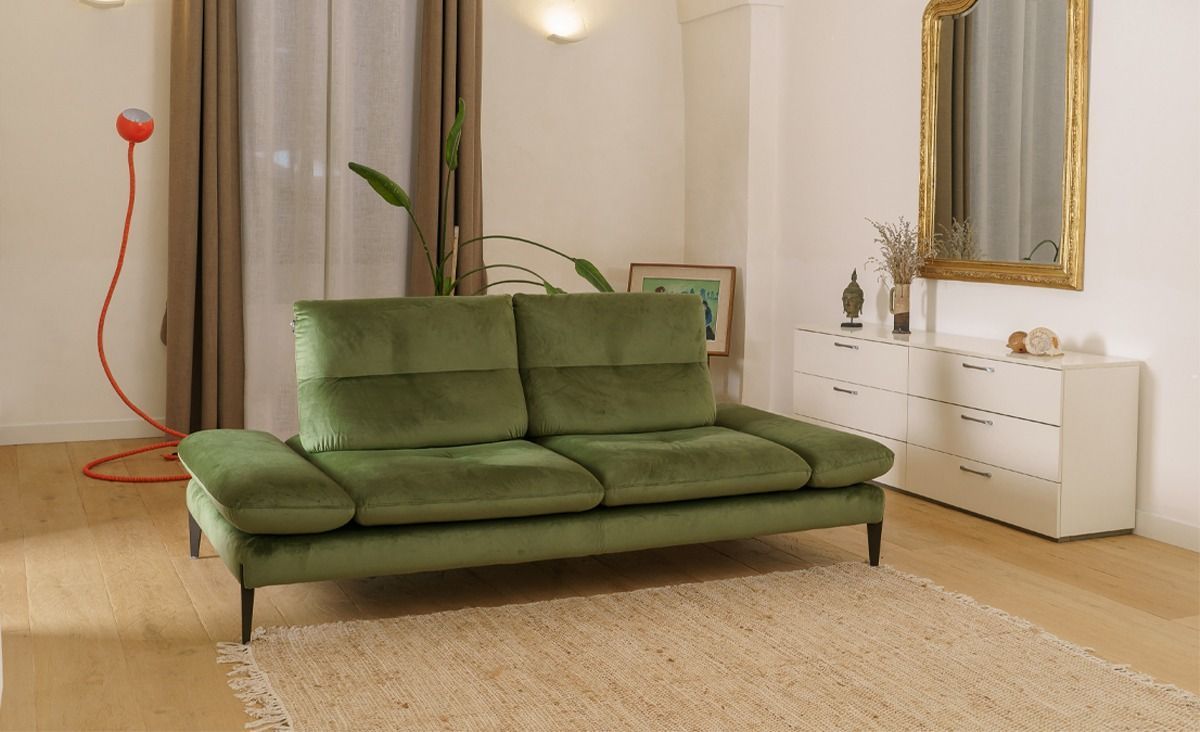 Divanetto verde in un luminoso soggiorno con specchio, cassettiera bianca e tappeto beige.