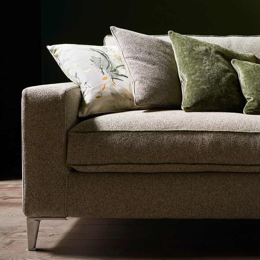 Primo piano di un divano marrone con cuscini decorativi a fantasia e verdi, illuminato da una luce soffusa.