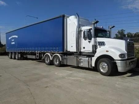 A Semi Truck with A Blue Container on The Back Is Driving Down a Road — Smillie Transport Pty Ltd in Toowoomba, QLD
