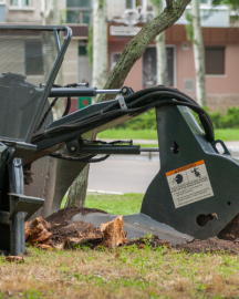A stump grinder machine grinds away a tree stump in a grassy area near a building.