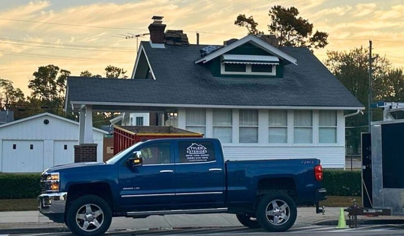 Blue pickup truck parked in front of a house with a new dark gray roof. Sky is dusky.