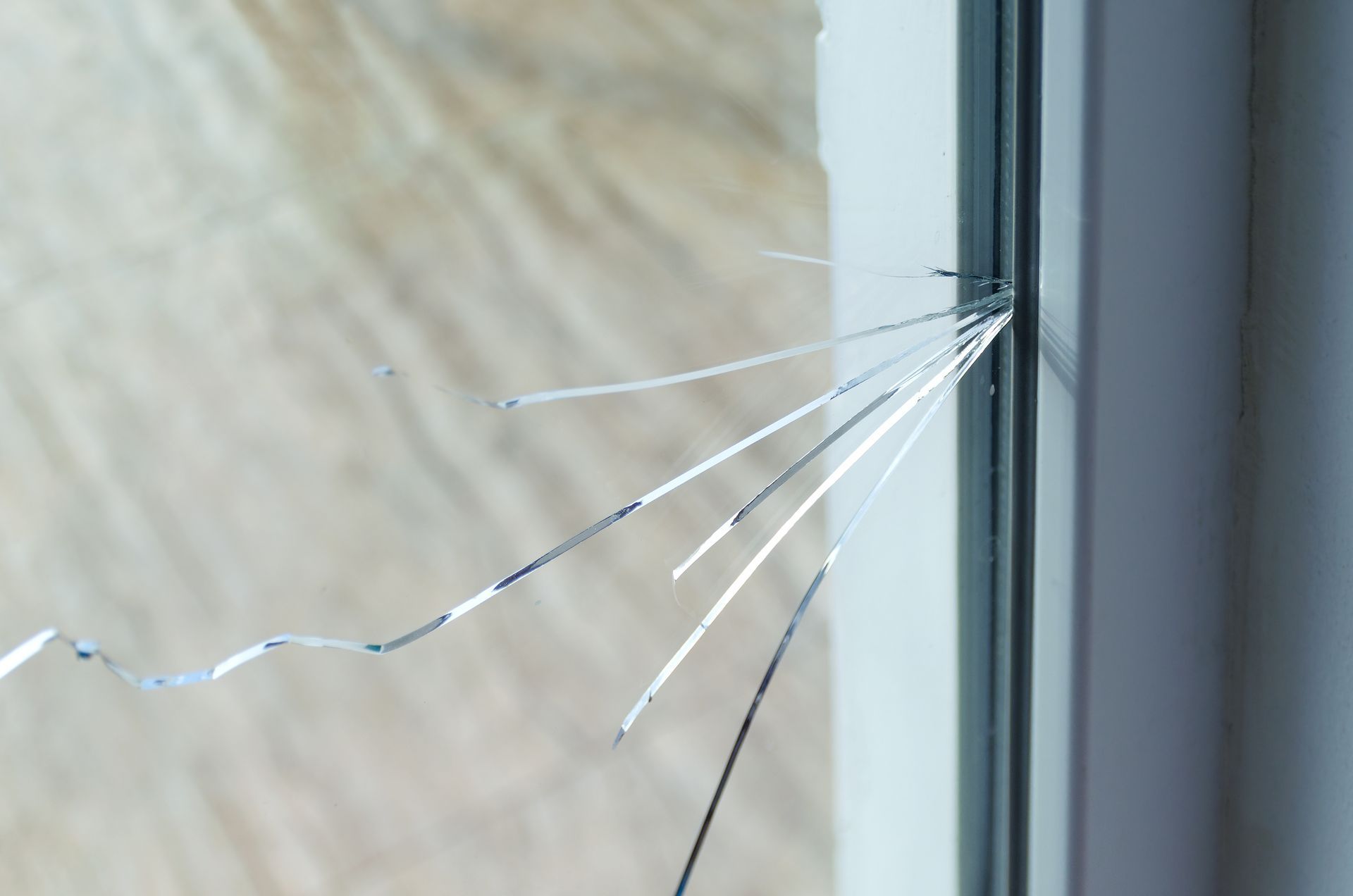 Cracked glass window pane with fractures radiating from the edge, next to white frame.