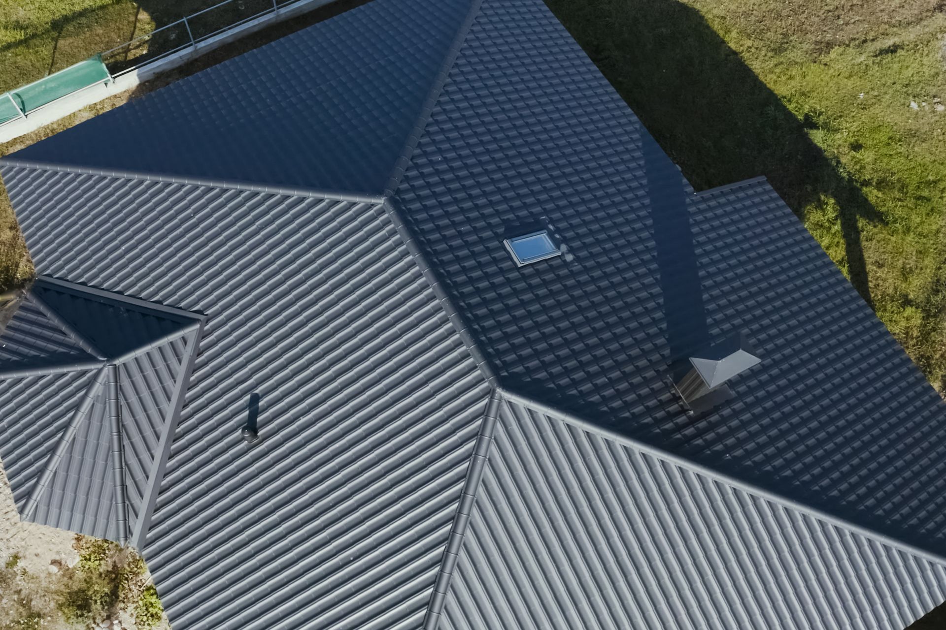 Dark gray metal roof on a multi-sectioned house, featuring a chimney, skylight, and distinct ridges.