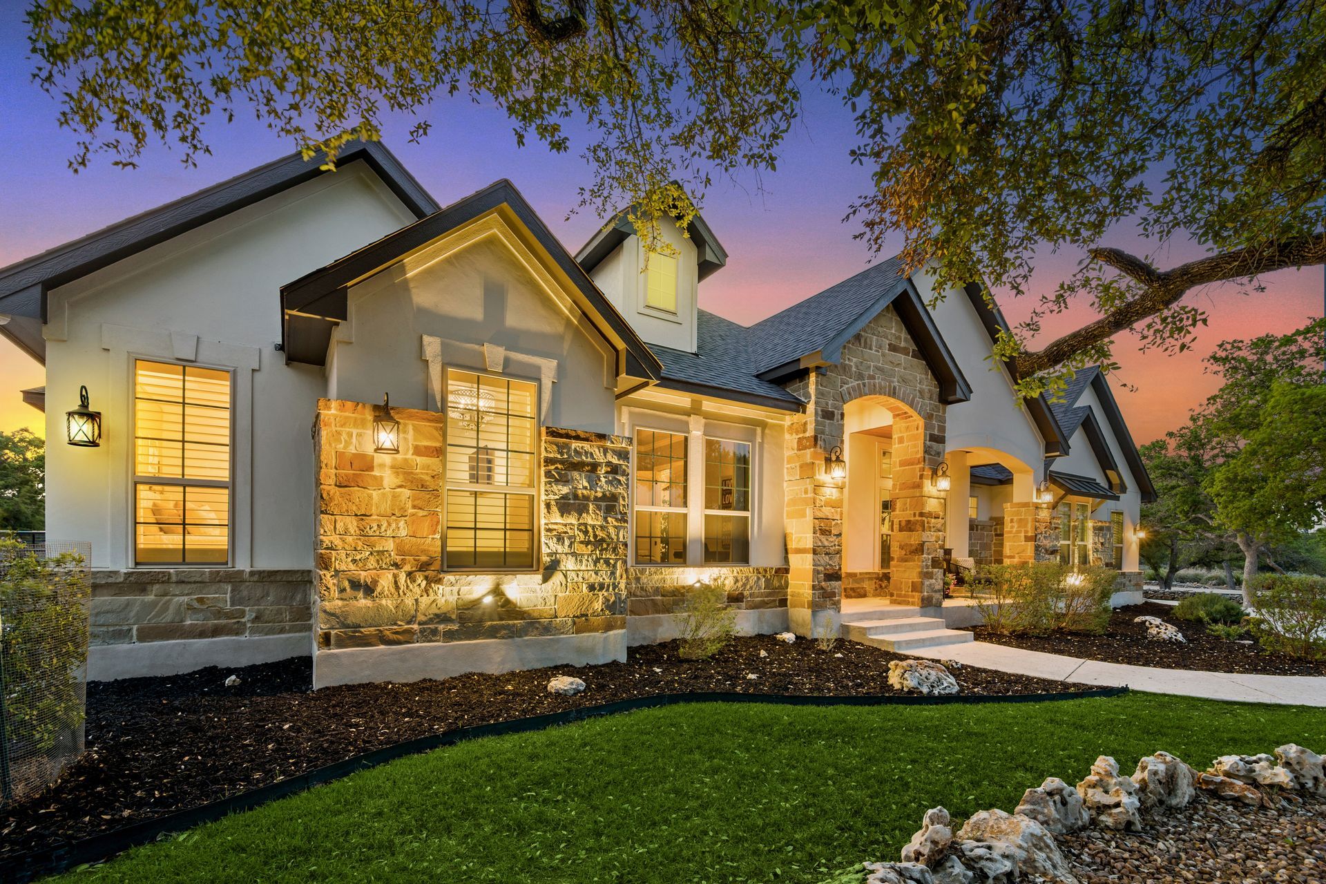 Upscale home exterior with stone accents and manicured lawn at sunset.