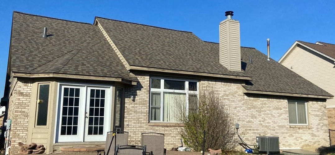 A brick house with a dark gray shingled roof, chimney, and French doors under a bright blue sky.