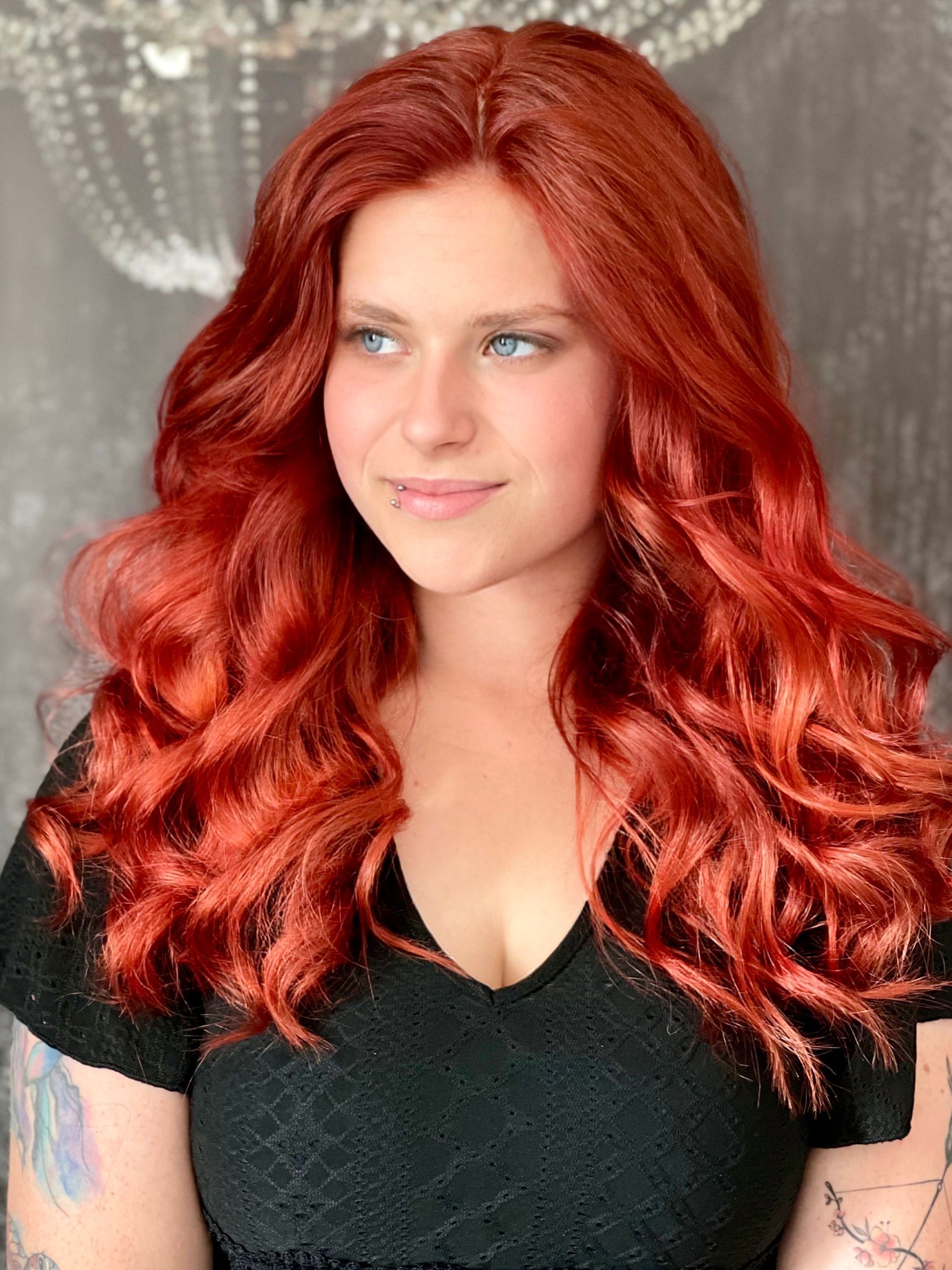 Eine Frau mit langen roten Haaren und blauen Augen trägt ein schwarzes Hemd.