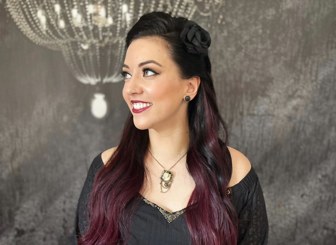 Eine Frau mit lila Haaren trägt ein schwarzes Kleid und eine Halskette.
