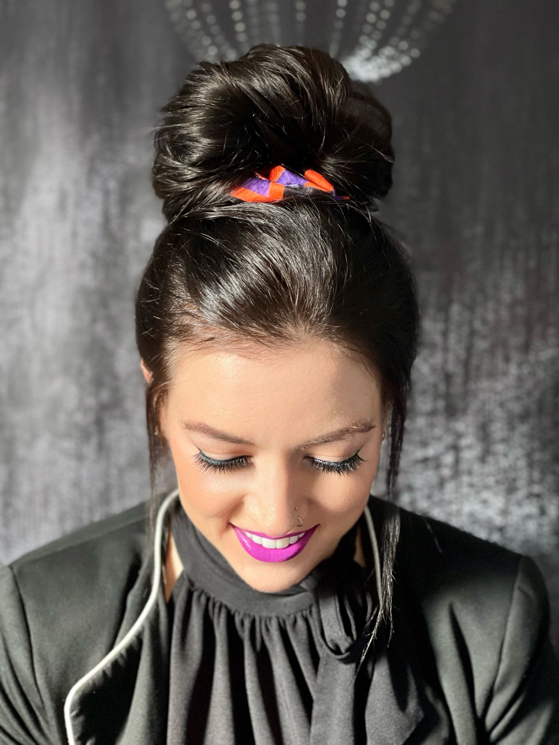 Eine Frau mit einem Haarknoten und lila Lippenstift lächelt.