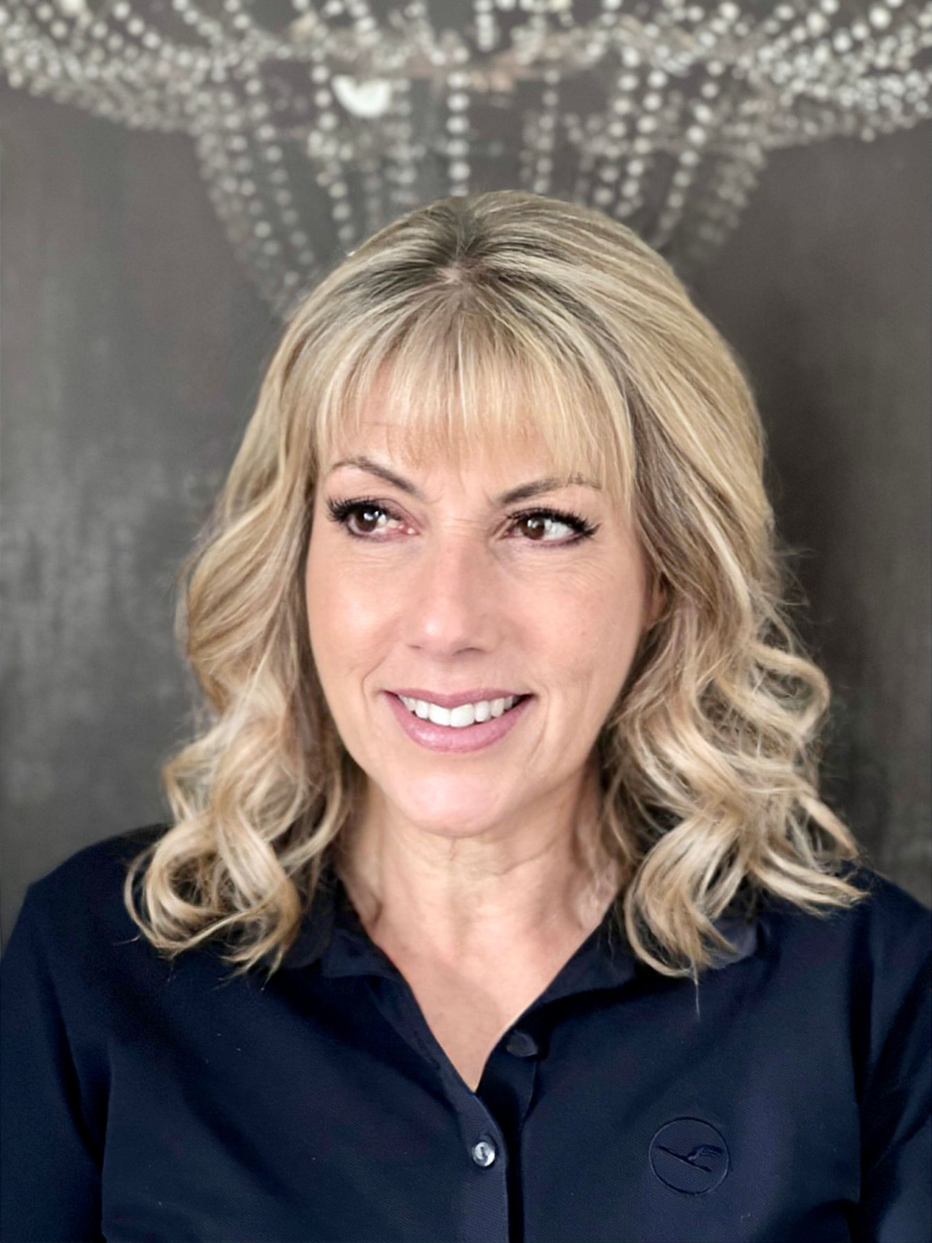 Eine Frau mit blonden Haaren trägt ein blaues Hemd und lächelt.