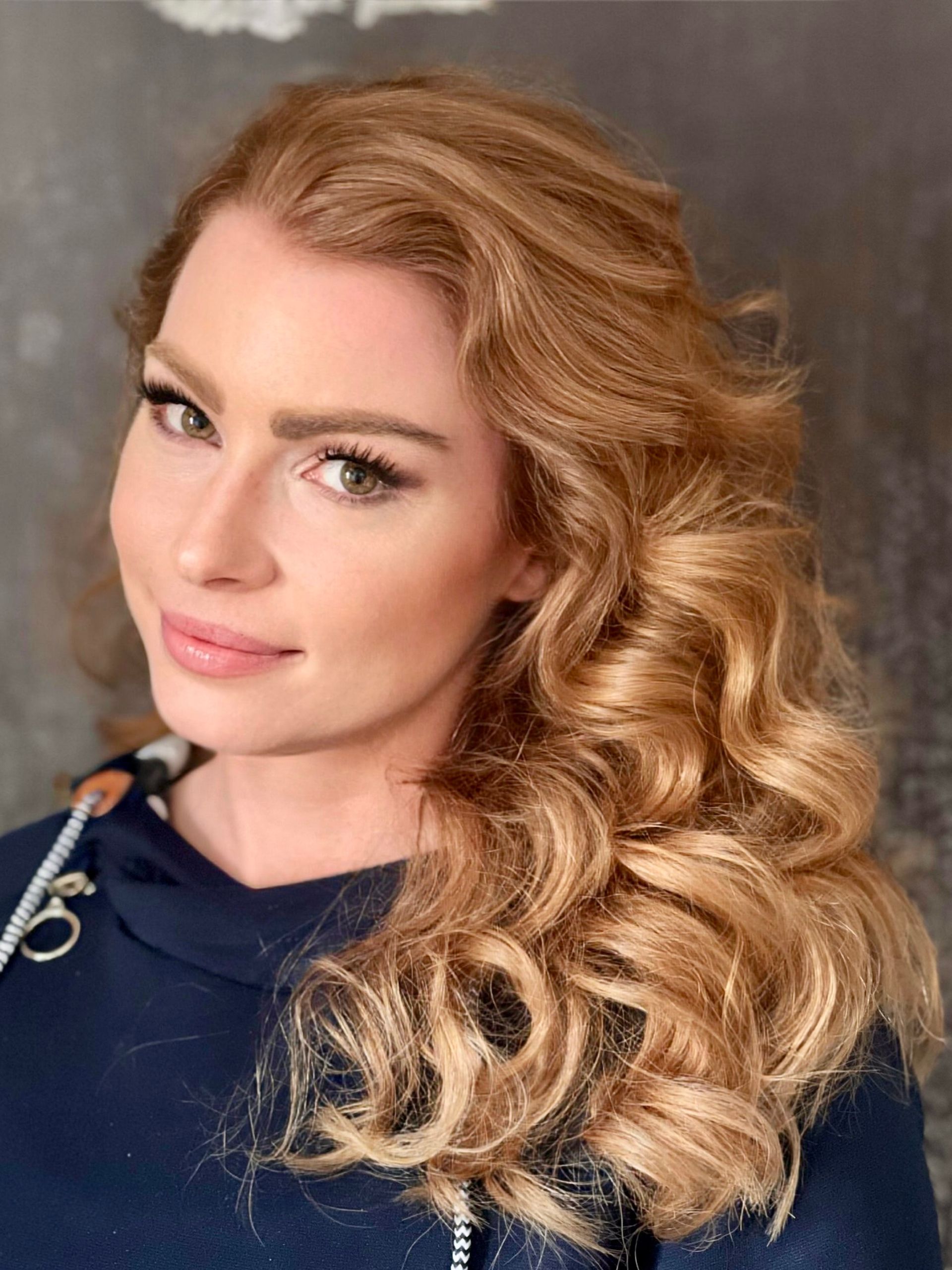 Eine Frau mit langen blonden Locken trägt ein blaues Hemd.