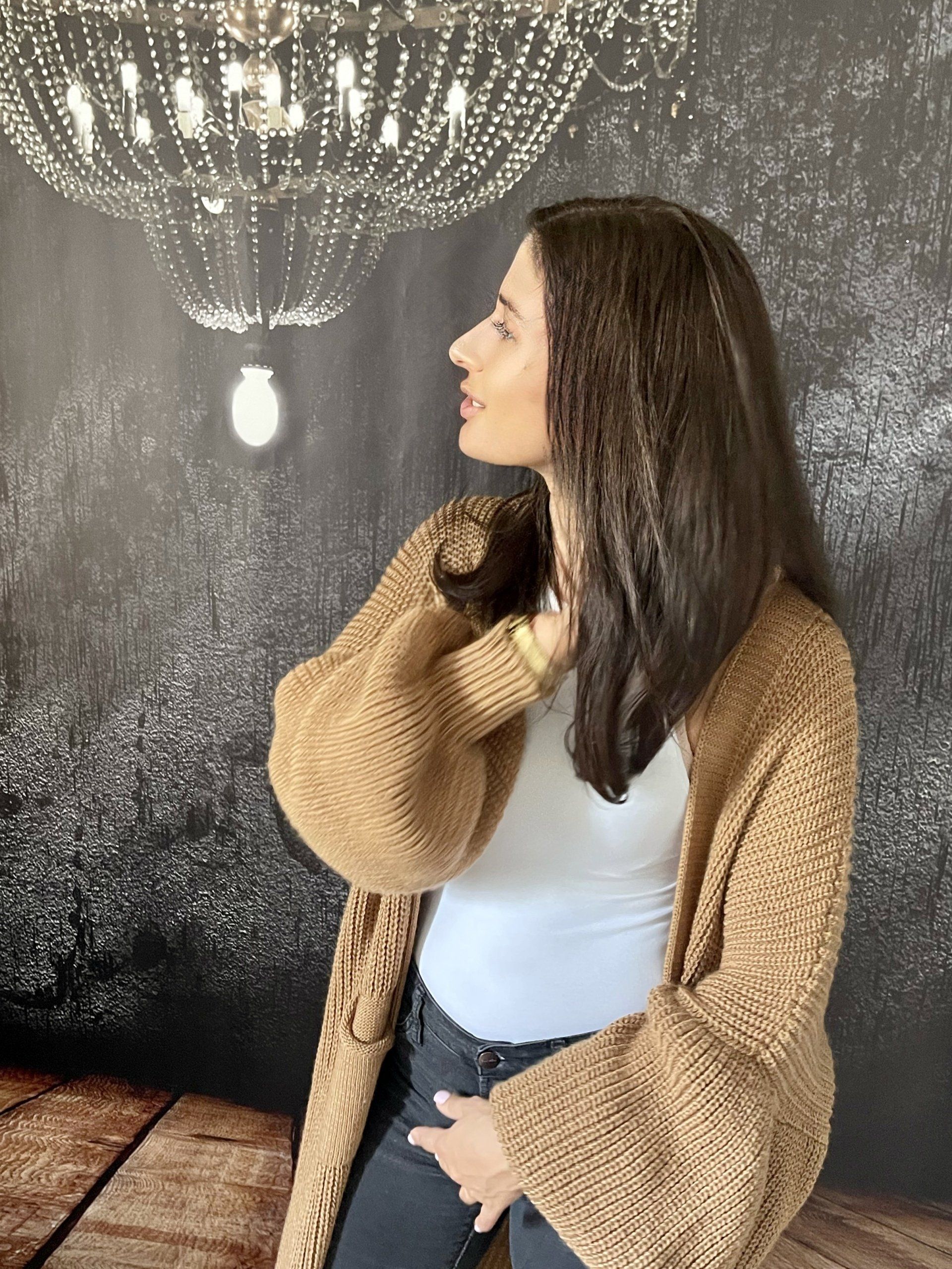 Eine Frau in einer braunen Strickjacke steht vor einem Kronleuchter.