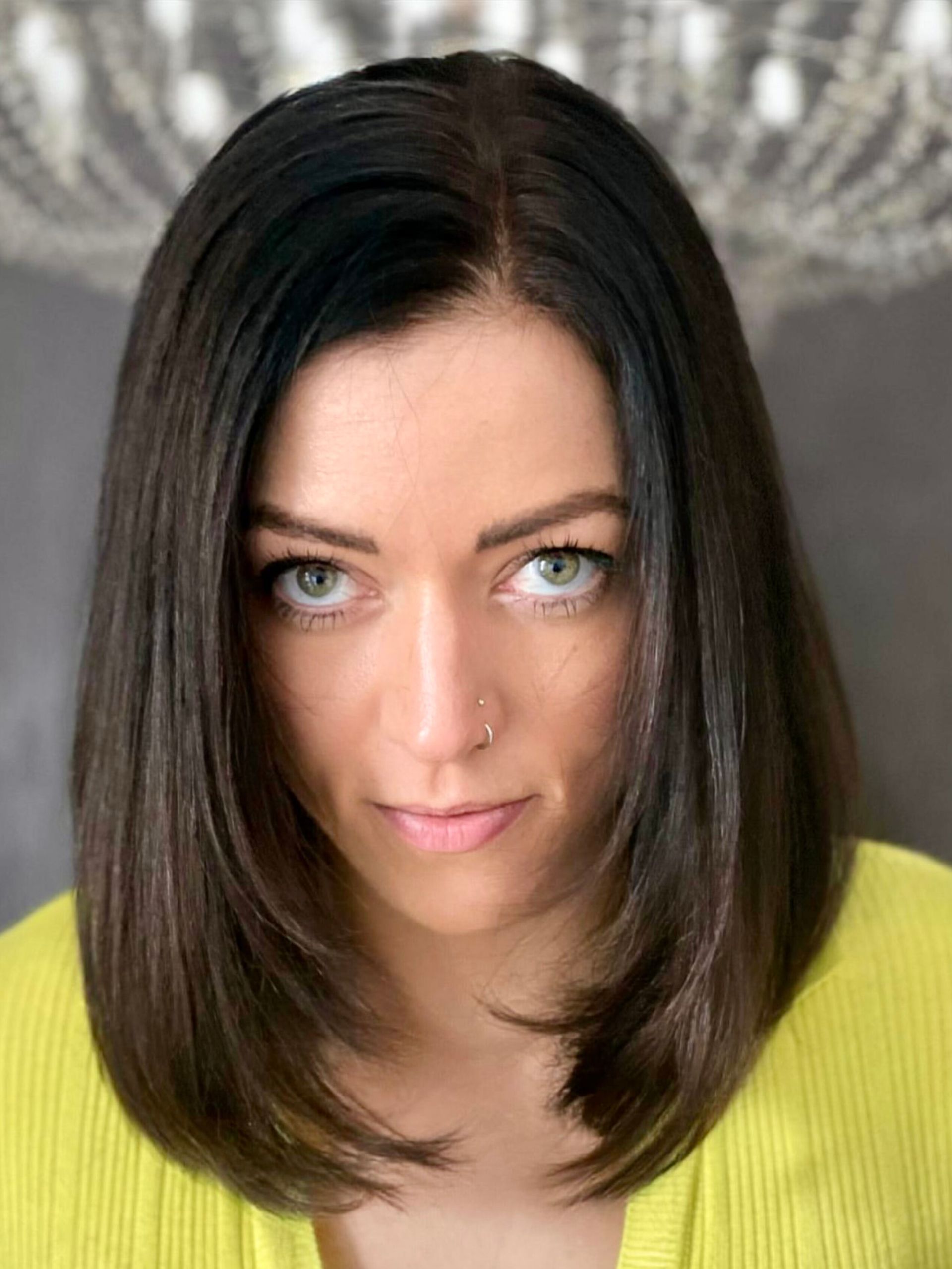 Eine Frau mit dunklem Haar trägt ein gelbes Hemd und schaut in die Kamera.
