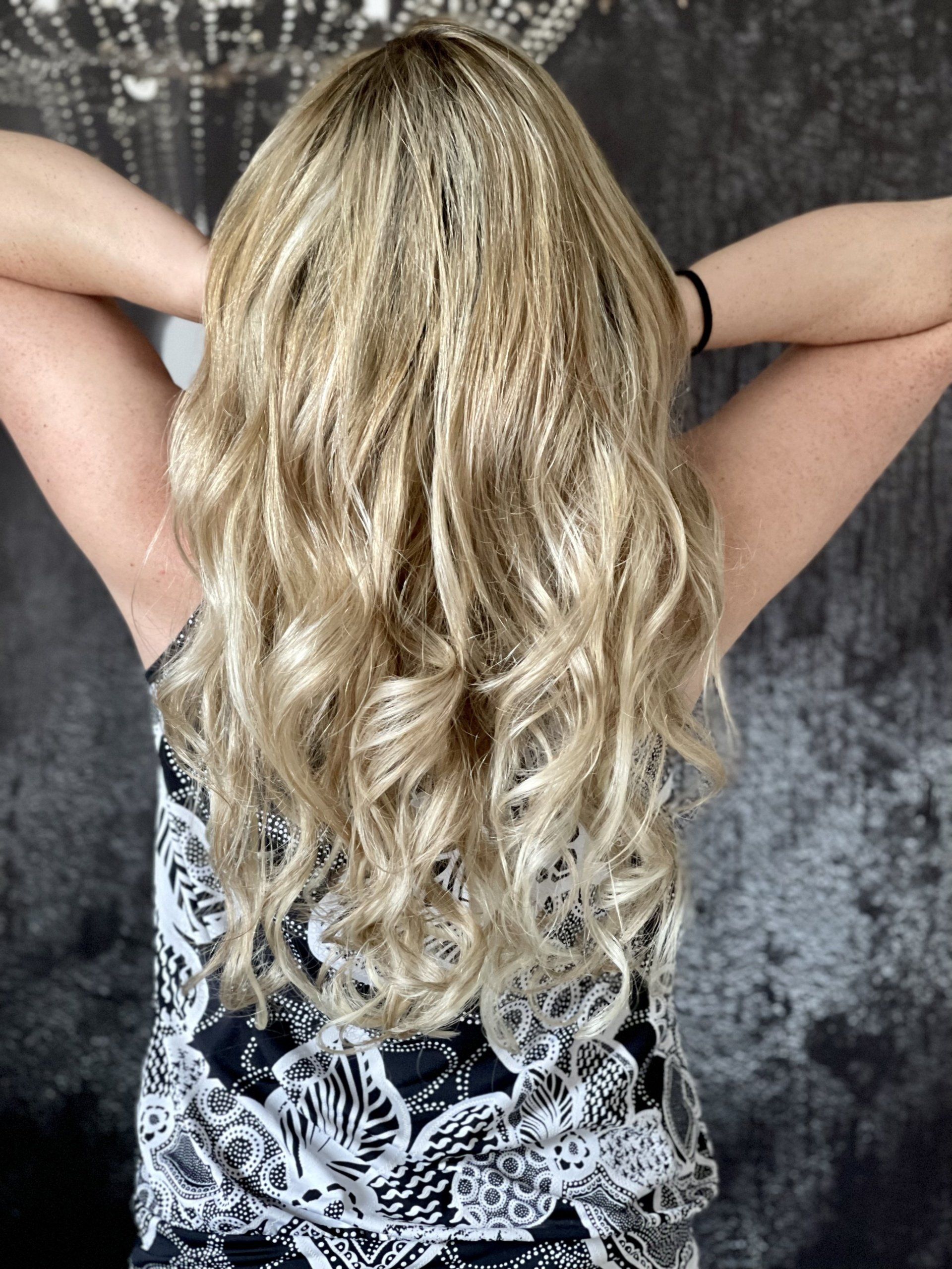 Eine Frau mit langen blonden Haaren steht mit den Händen hinter dem Kopf da.