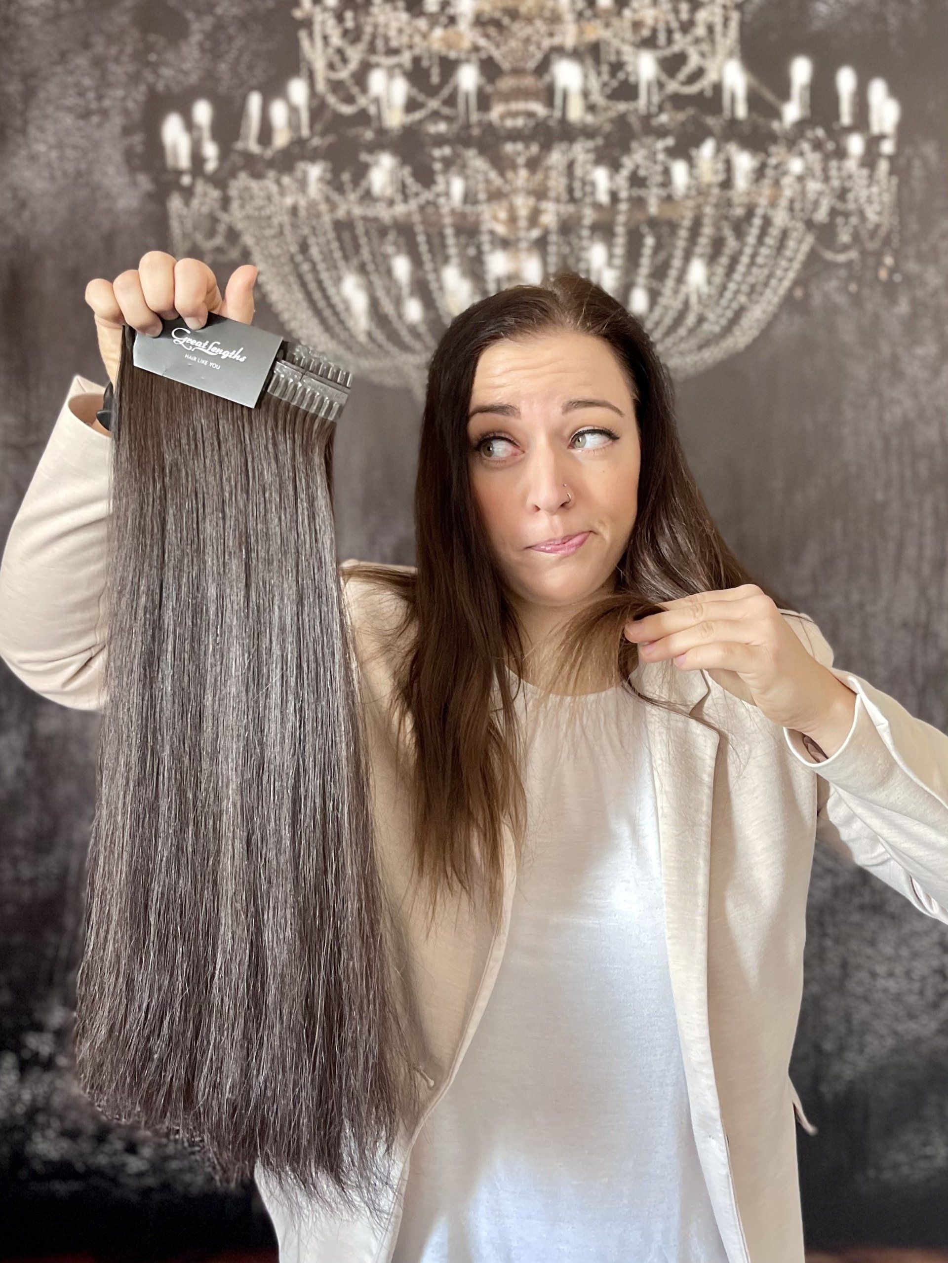 Eine Frau hält eine Bürste und eine Haarsträhne vor einem Kronleuchter.