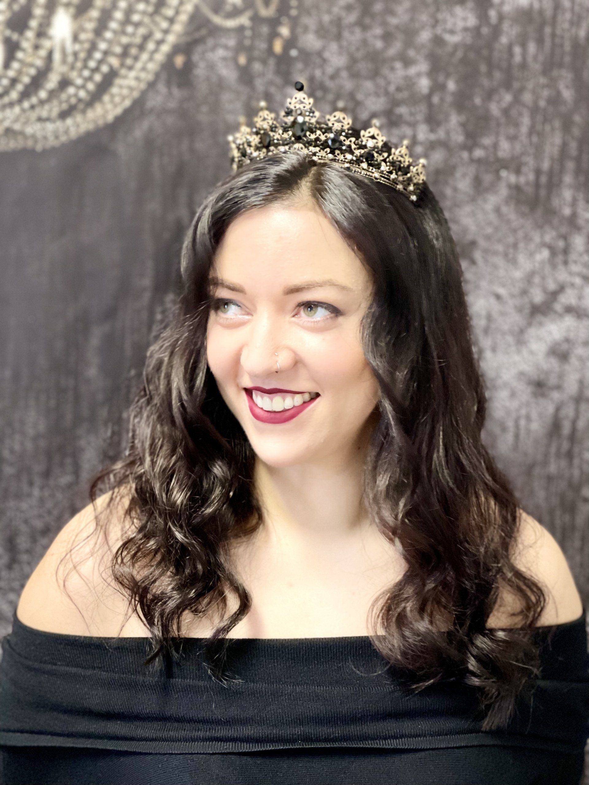 Eine Frau mit Tiara und schwarzem Kleid lächelt.
