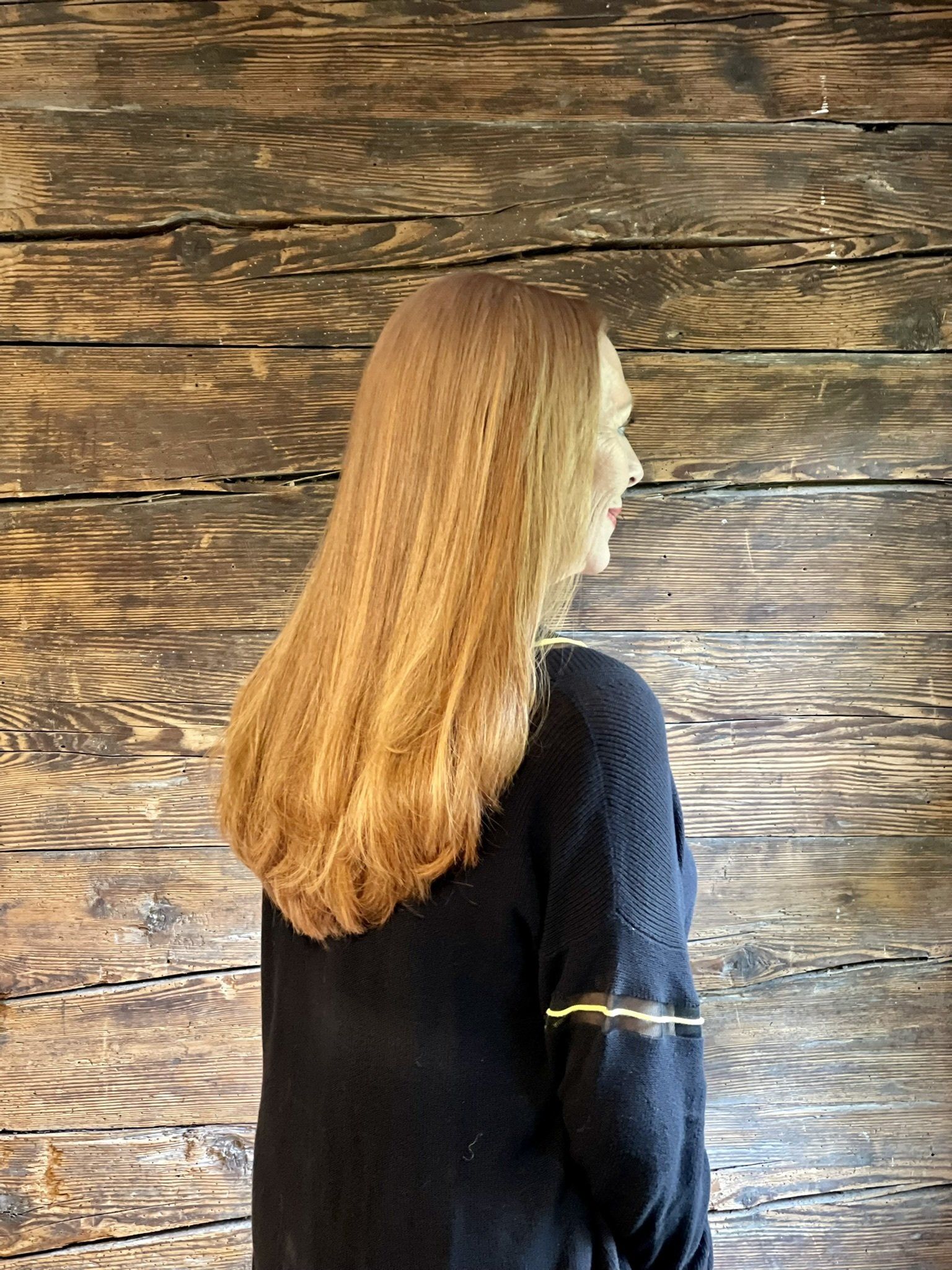 Eine Frau in einem schwarzen Pullover steht vor einer Holzwand.