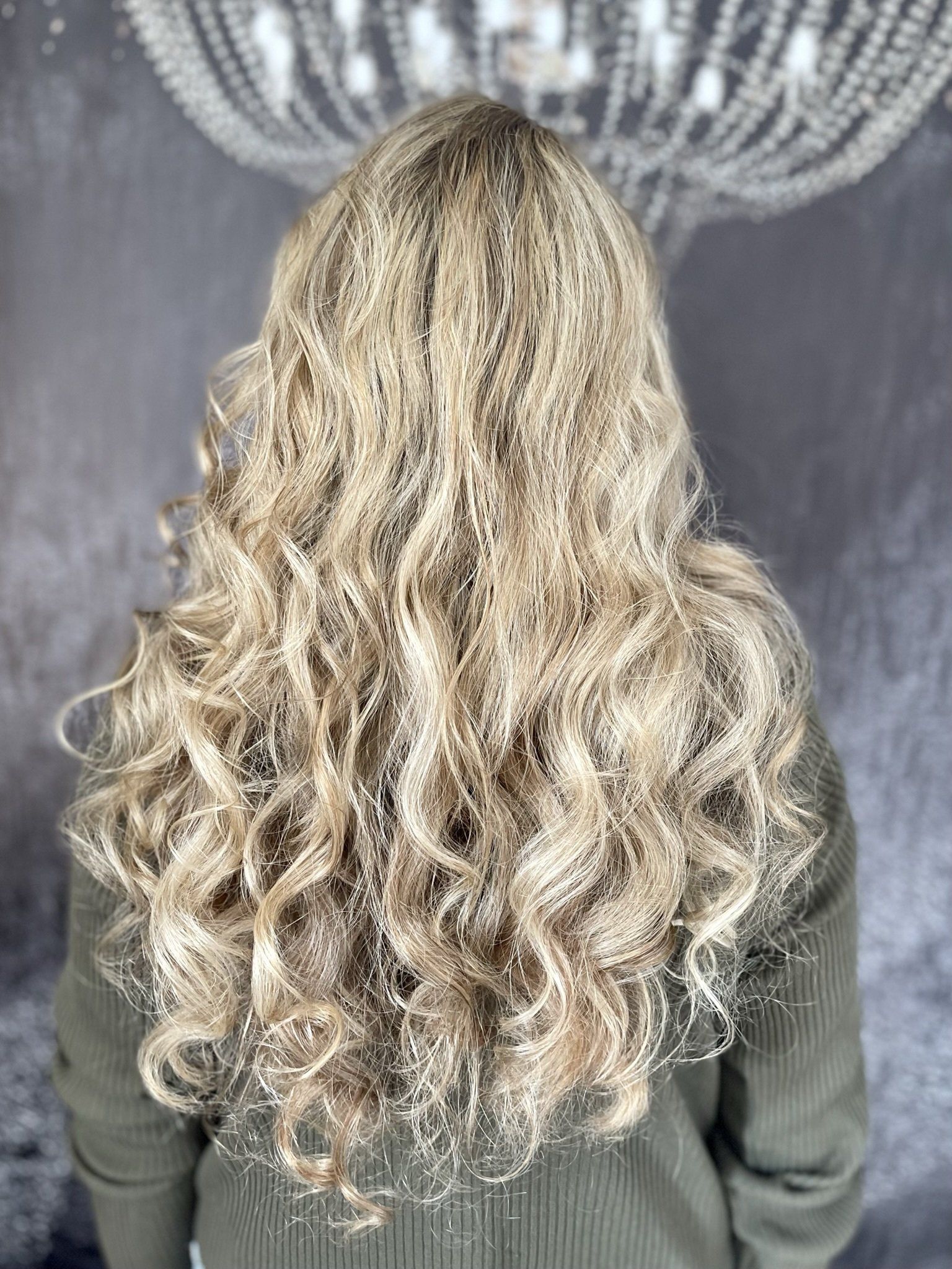 Eine Frau mit langen blonden Locken steht vor einem Kronleuchter.