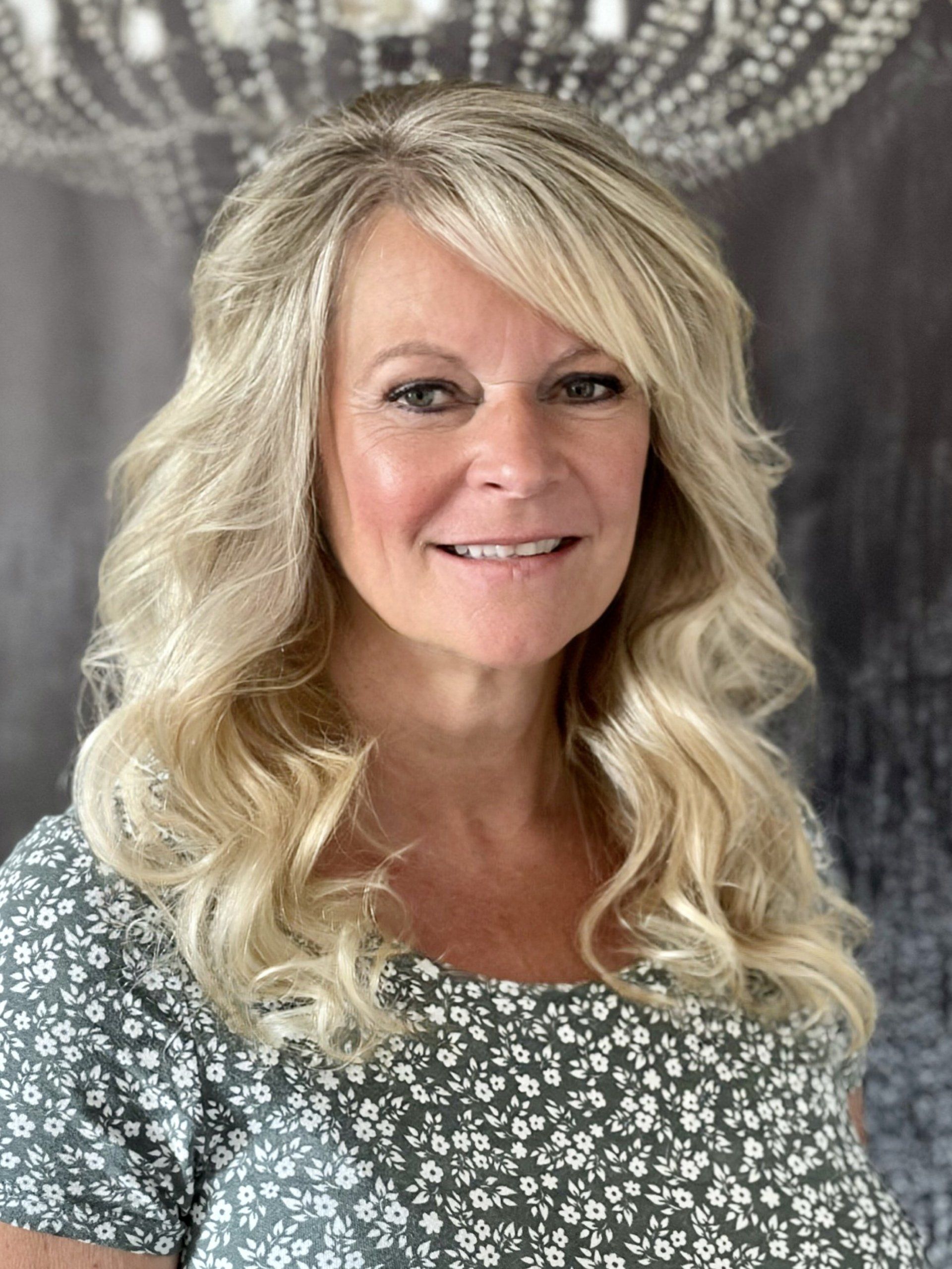 Eine Frau mit blonden Haaren trägt ein grünes Hemd mit Blumenmuster und lächelt.