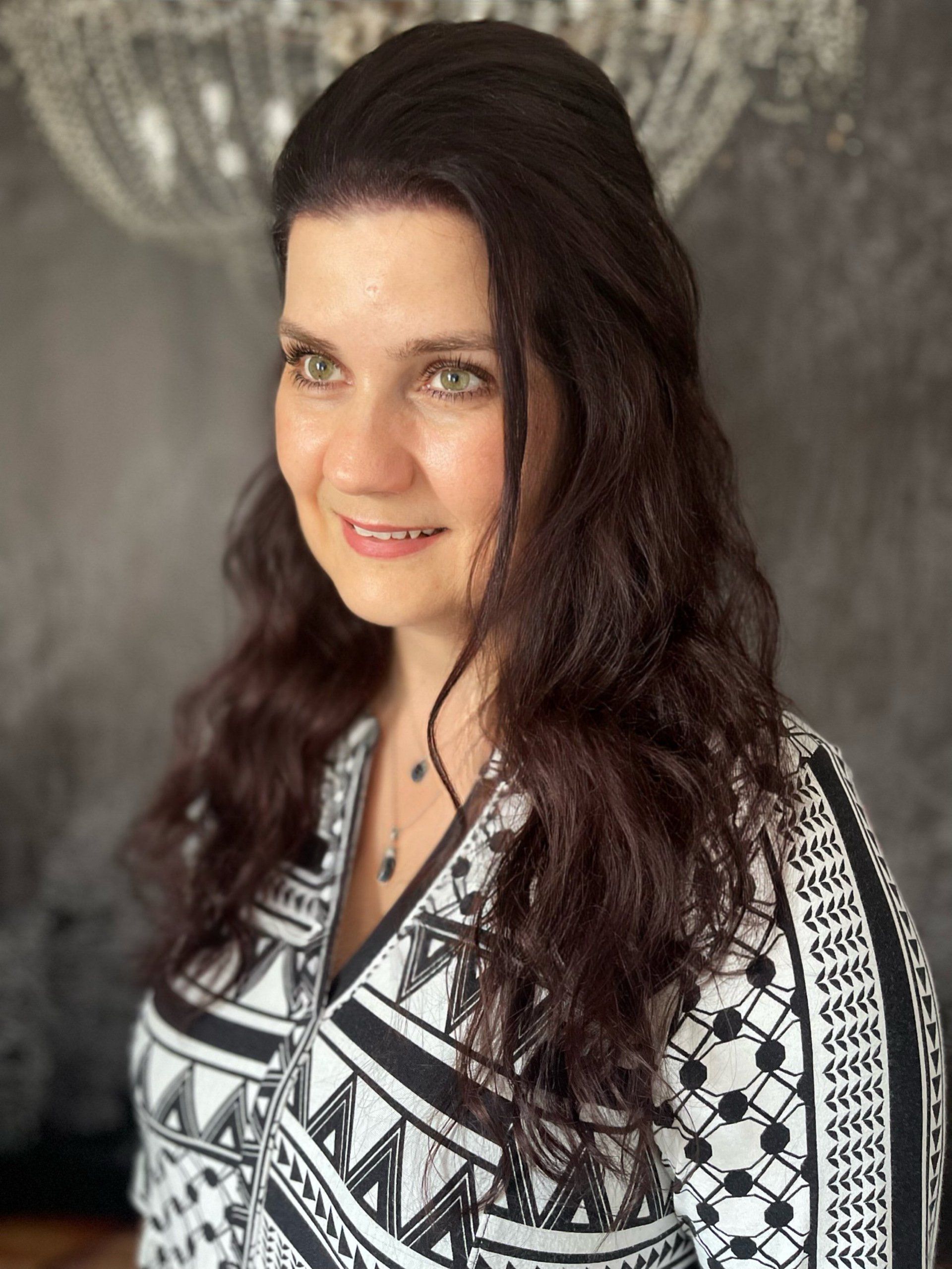 Eine Frau mit langen Haaren trägt ein schwarz-weißes Hemd und lächelt.