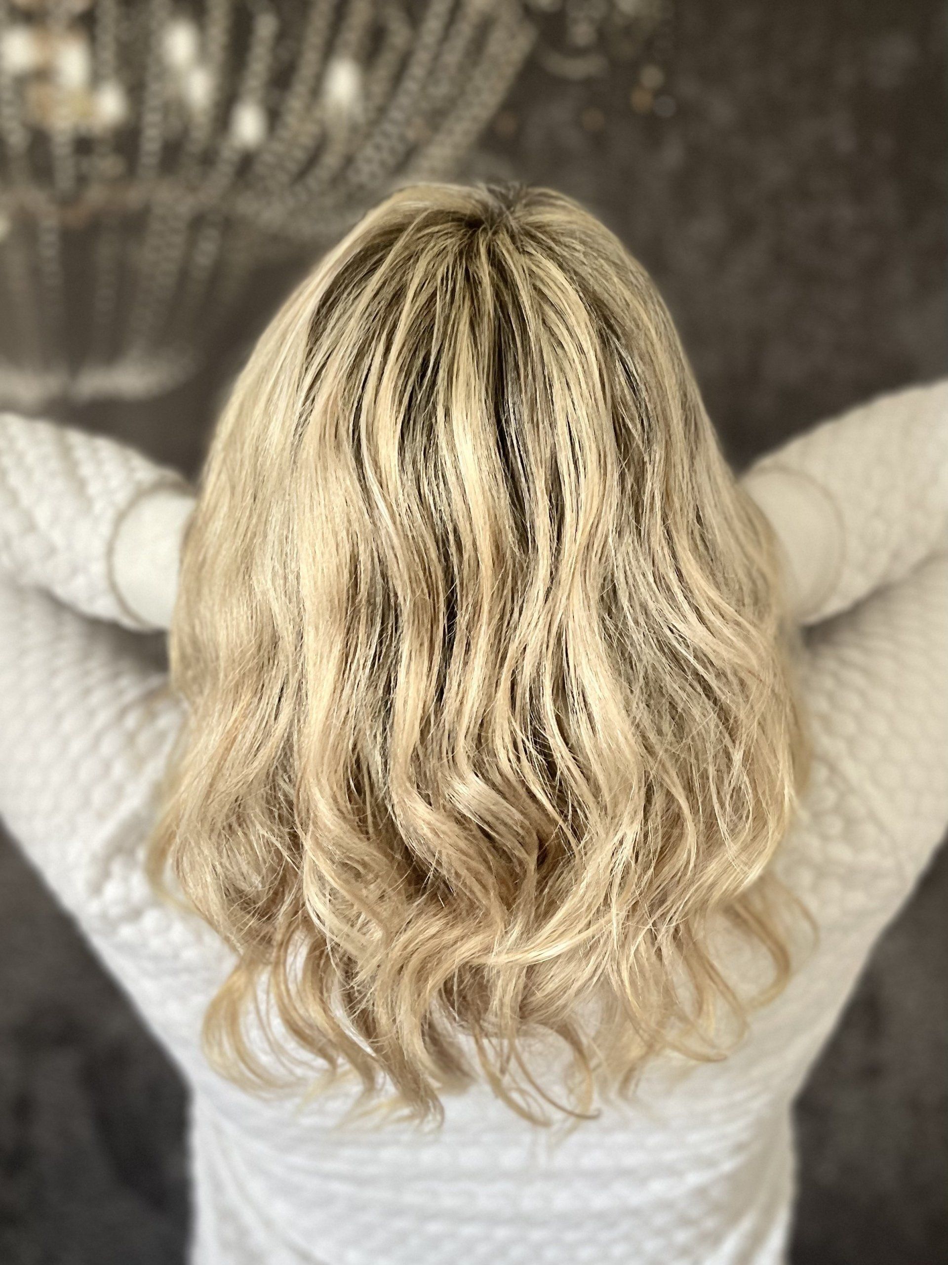 Eine Frau mit blonden Haaren steht mit ausgestreckten Armen vor einem Kronleuchter.