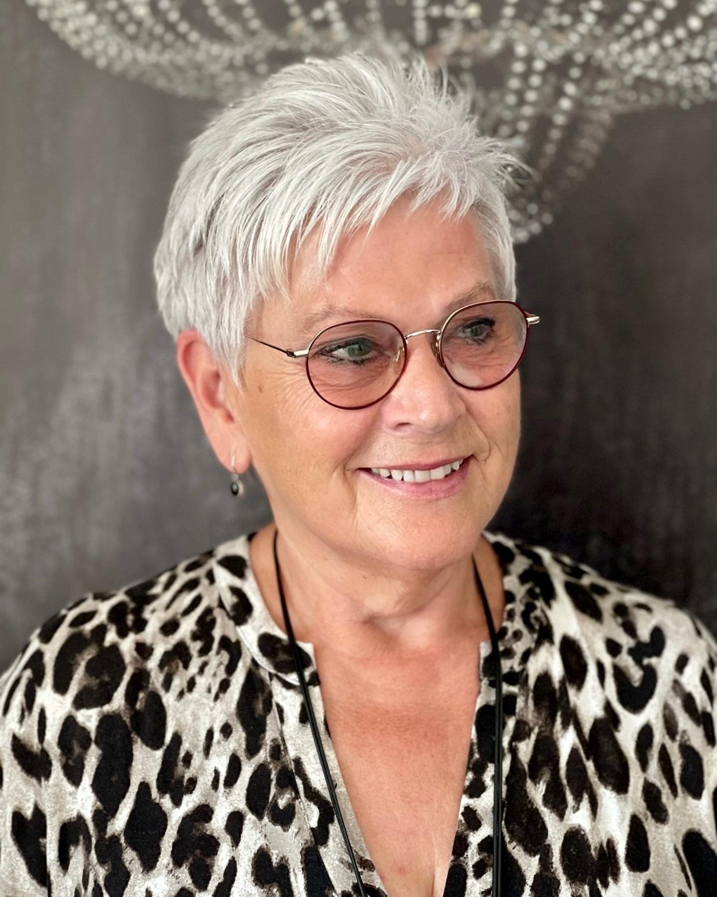 Eine Frau mit Brille und Hemd mit Leopardenmuster lächelt.