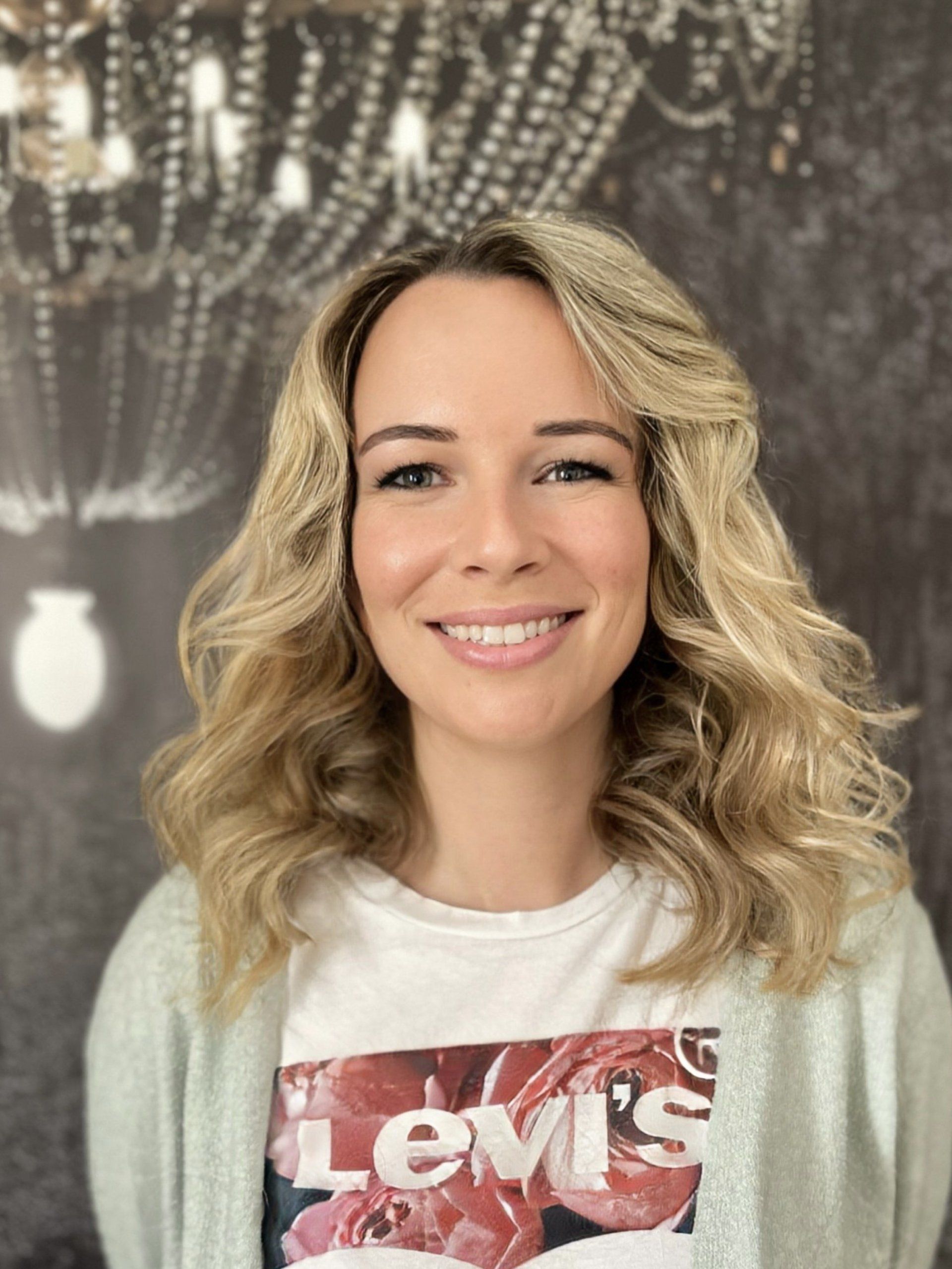 Eine Frau in einem Levis-T-Shirt lächelt vor einem Kronleuchter.