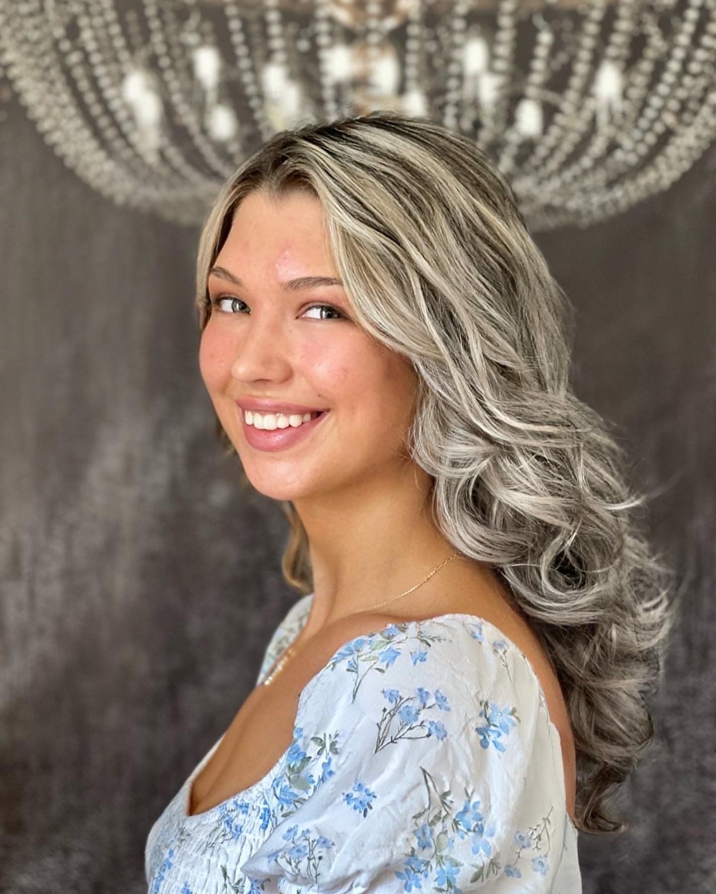Eine Frau mit langen blonden Haaren lächelt vor einem Kronleuchter.