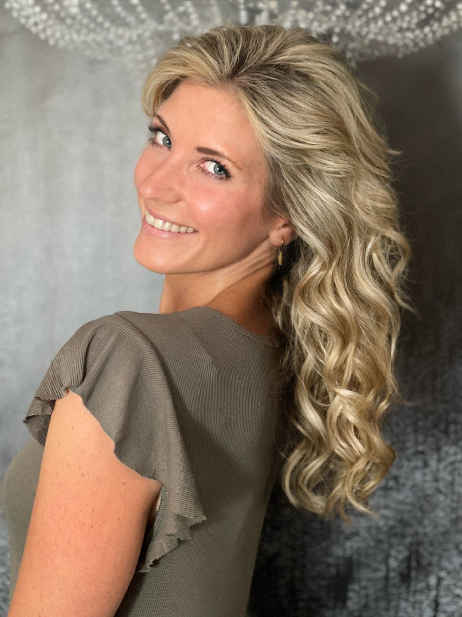 Eine Frau mit langen blonden Haaren lächelt und trägt ein grünes Hemd.