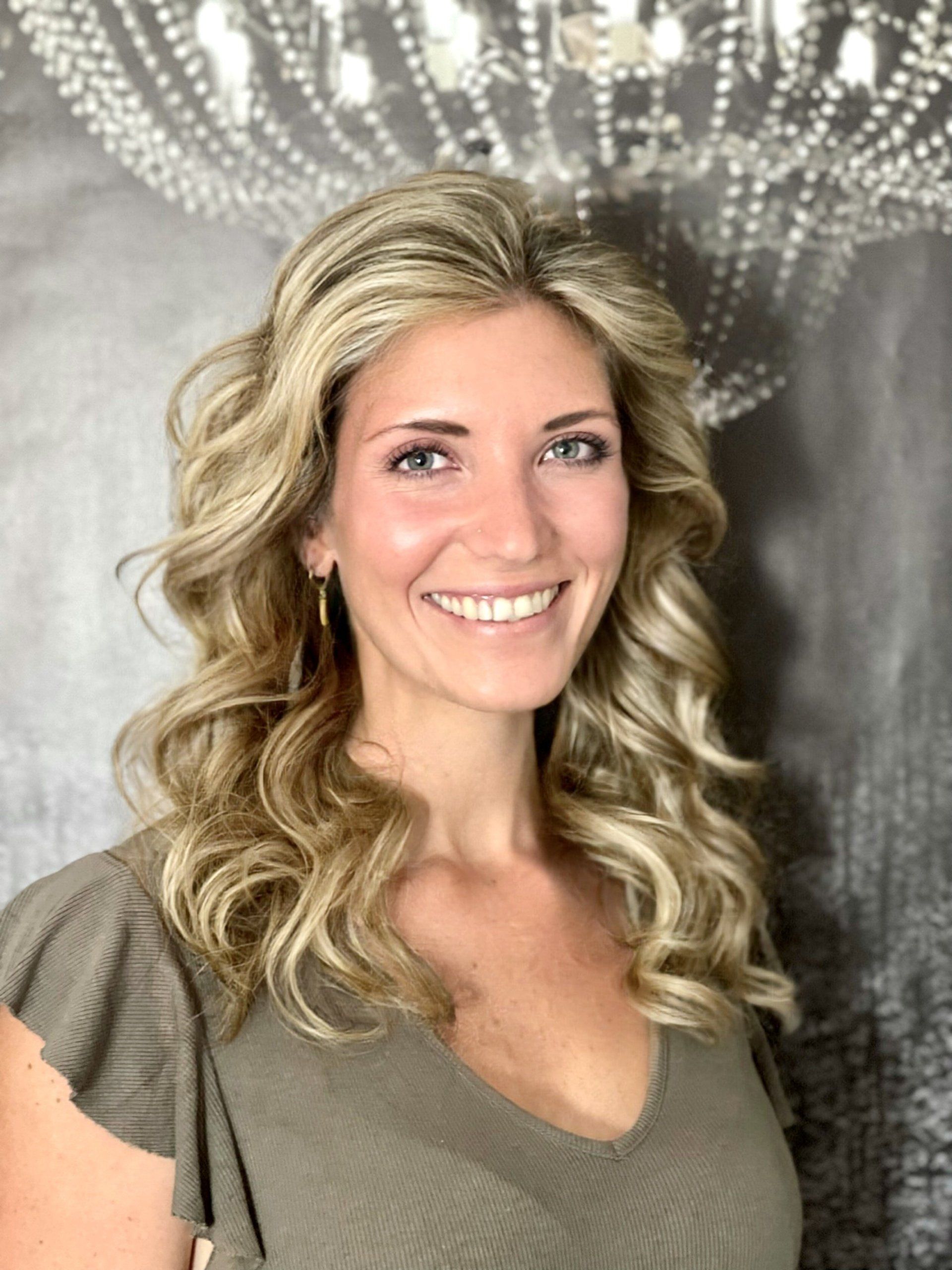 Eine Frau mit langen blonden Haaren lächelt vor einem Kronleuchter.