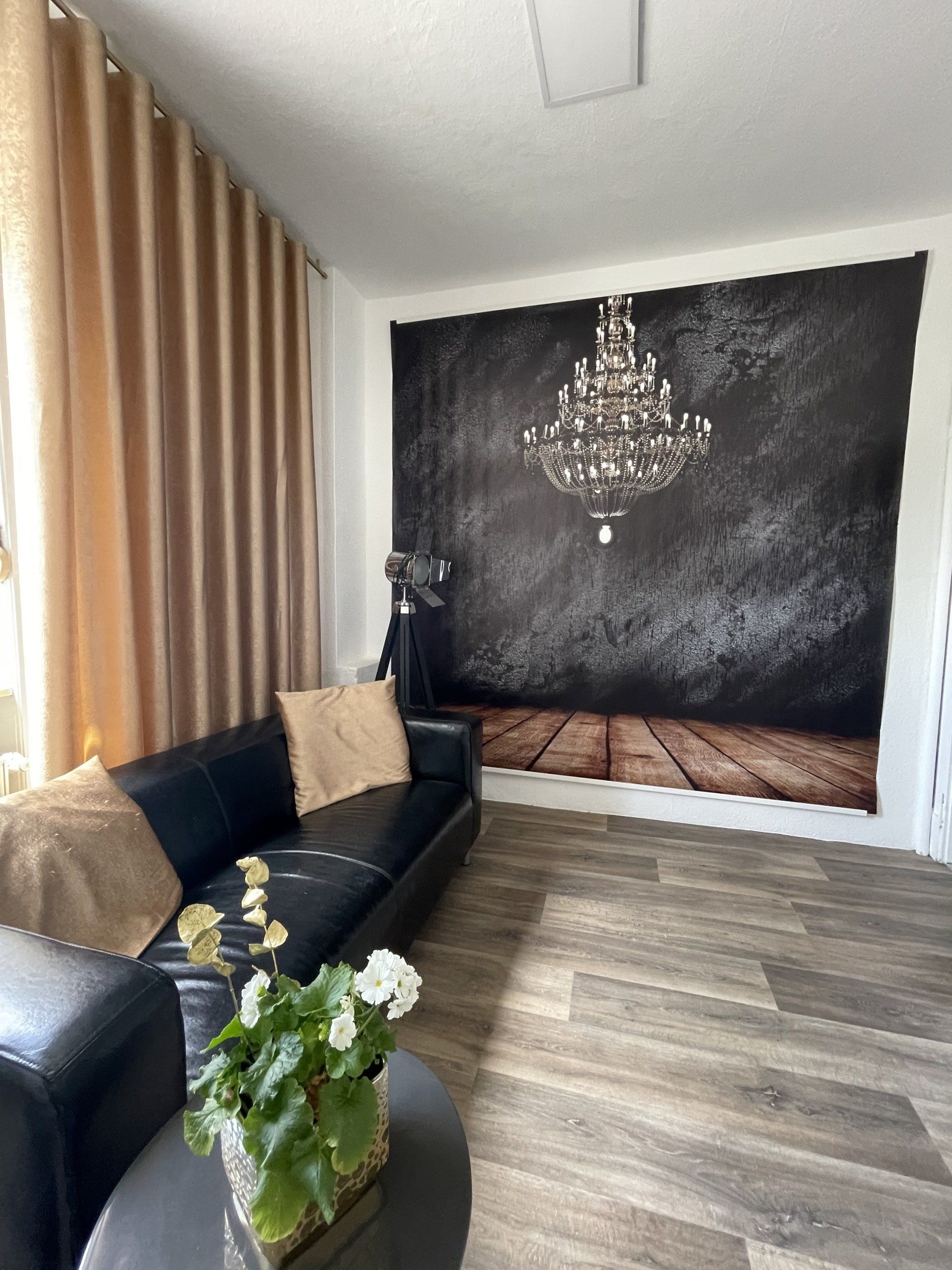 Ein Wohnzimmer mit einer schwarzen Couch und einem Kronleuchter, der von der Decke hängt.