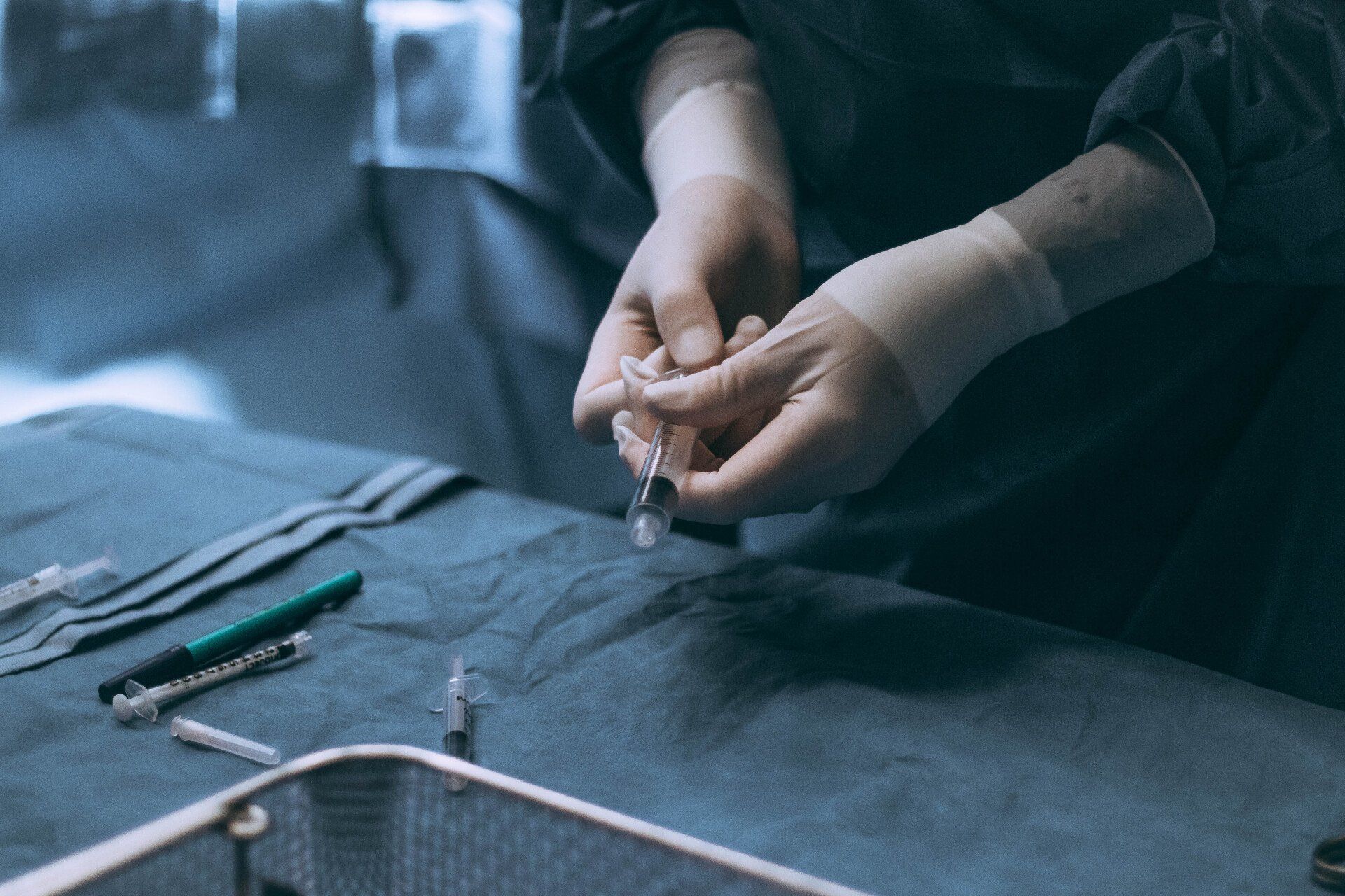 A person wearing gloves is holding a syringe on a table.
