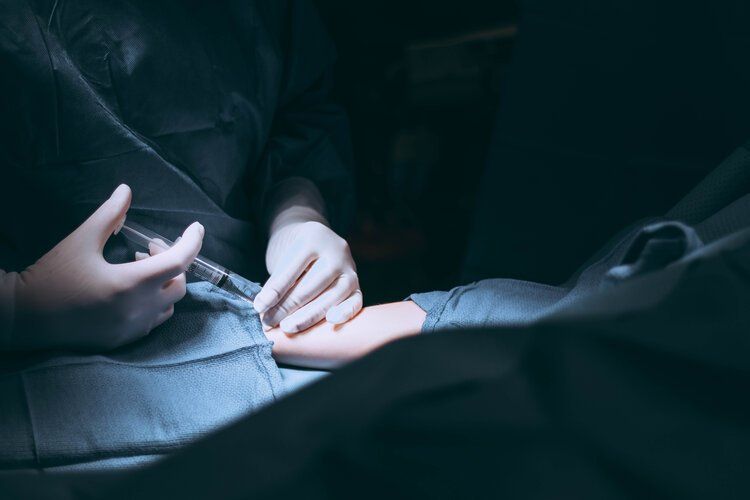 A surgeon is giving a patient an injection in their hand.