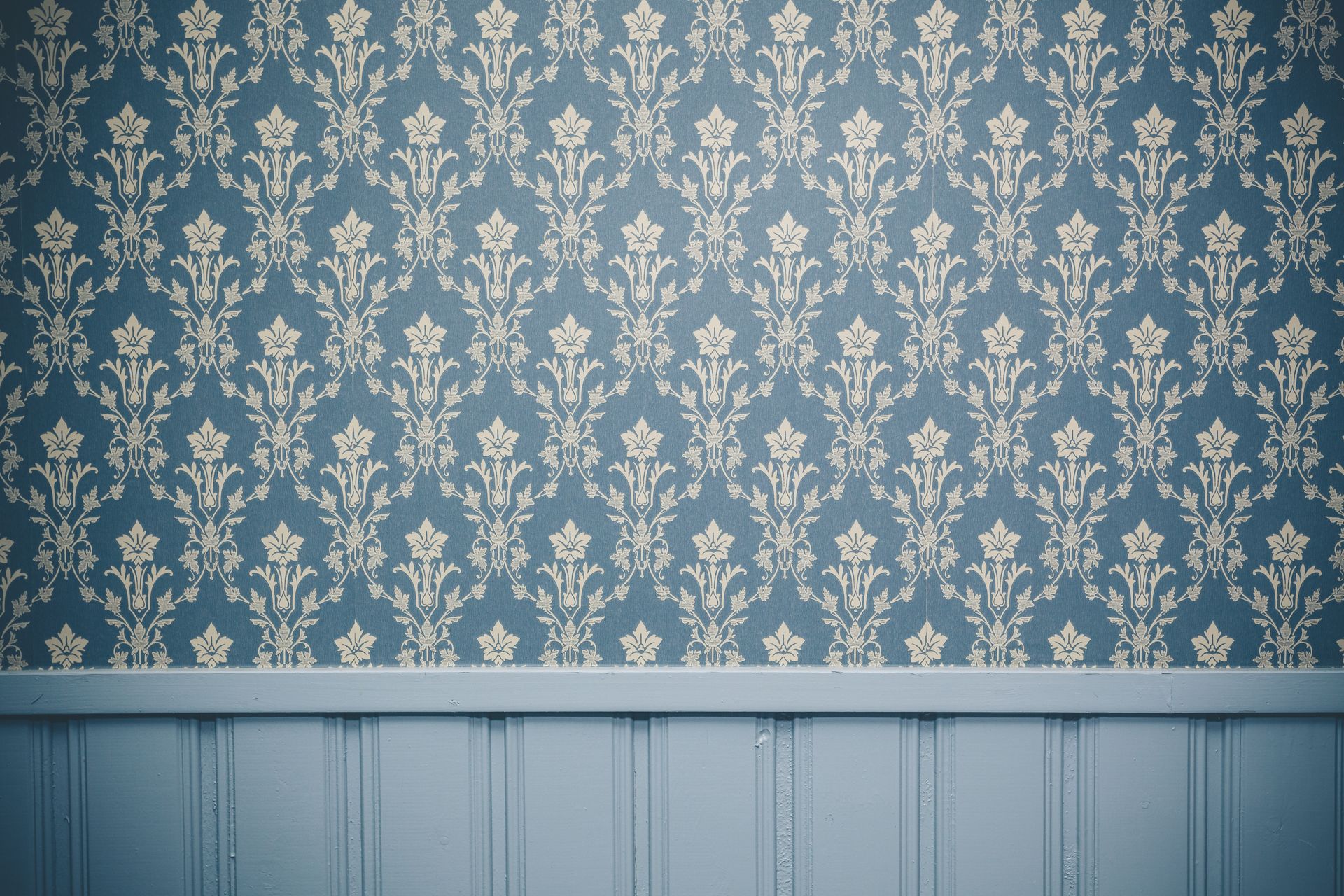 A blue wall with a patterned wallpaper and a wooden trim.