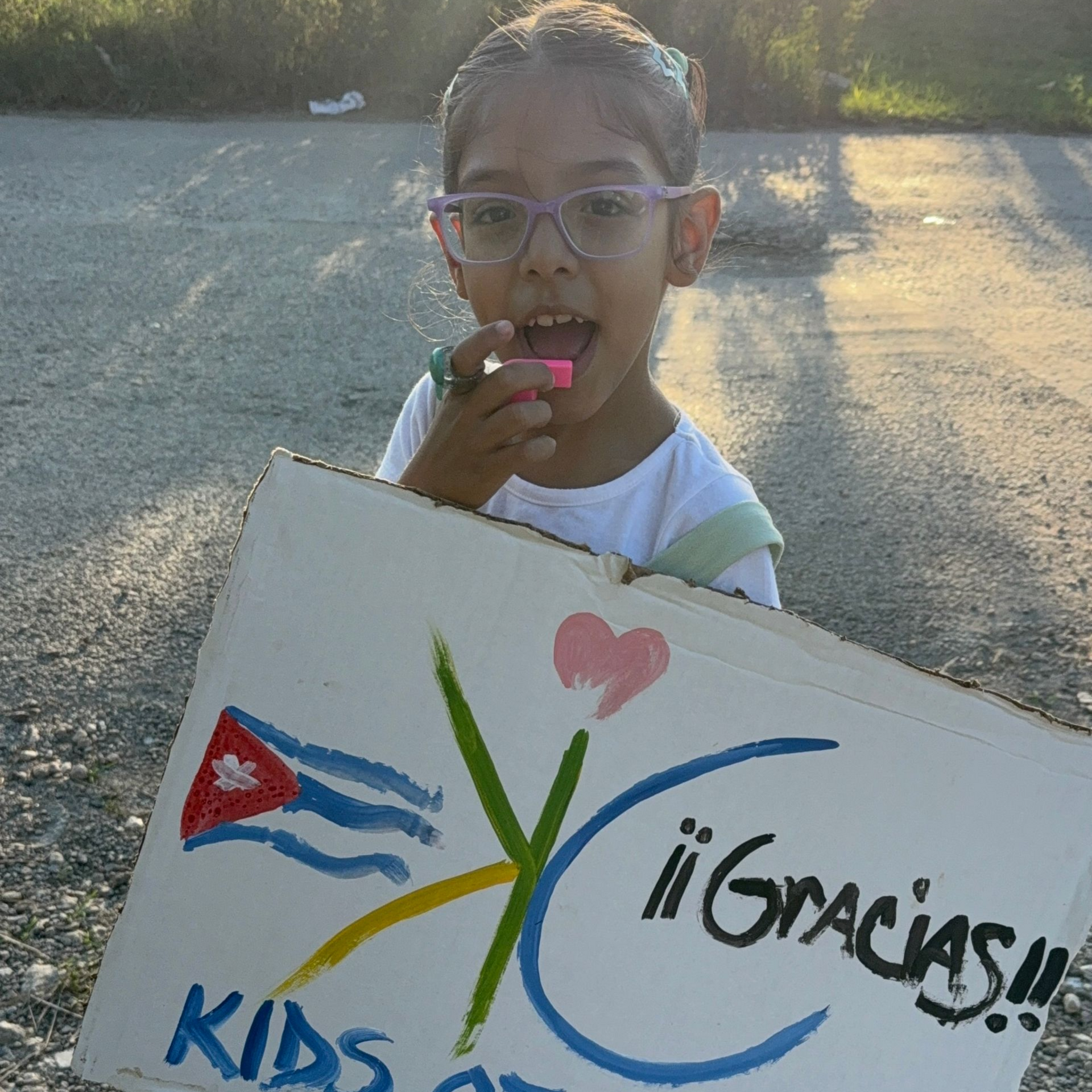 A person holds a cardboard sign featuring a Cuban flag, a heart, and the words