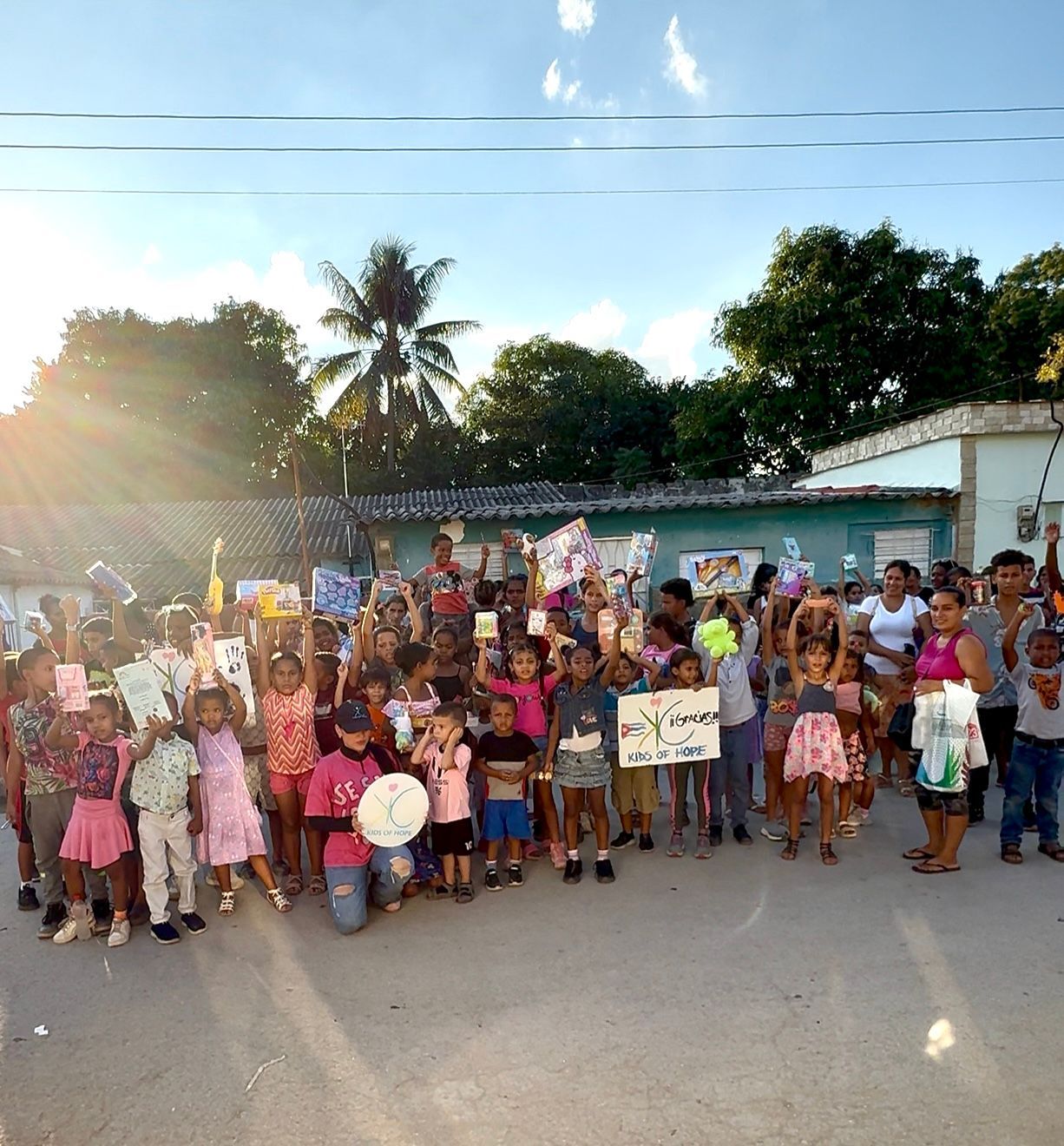 A group of people standing outdoors, many holding signs and crafts during a daytime community gathering.