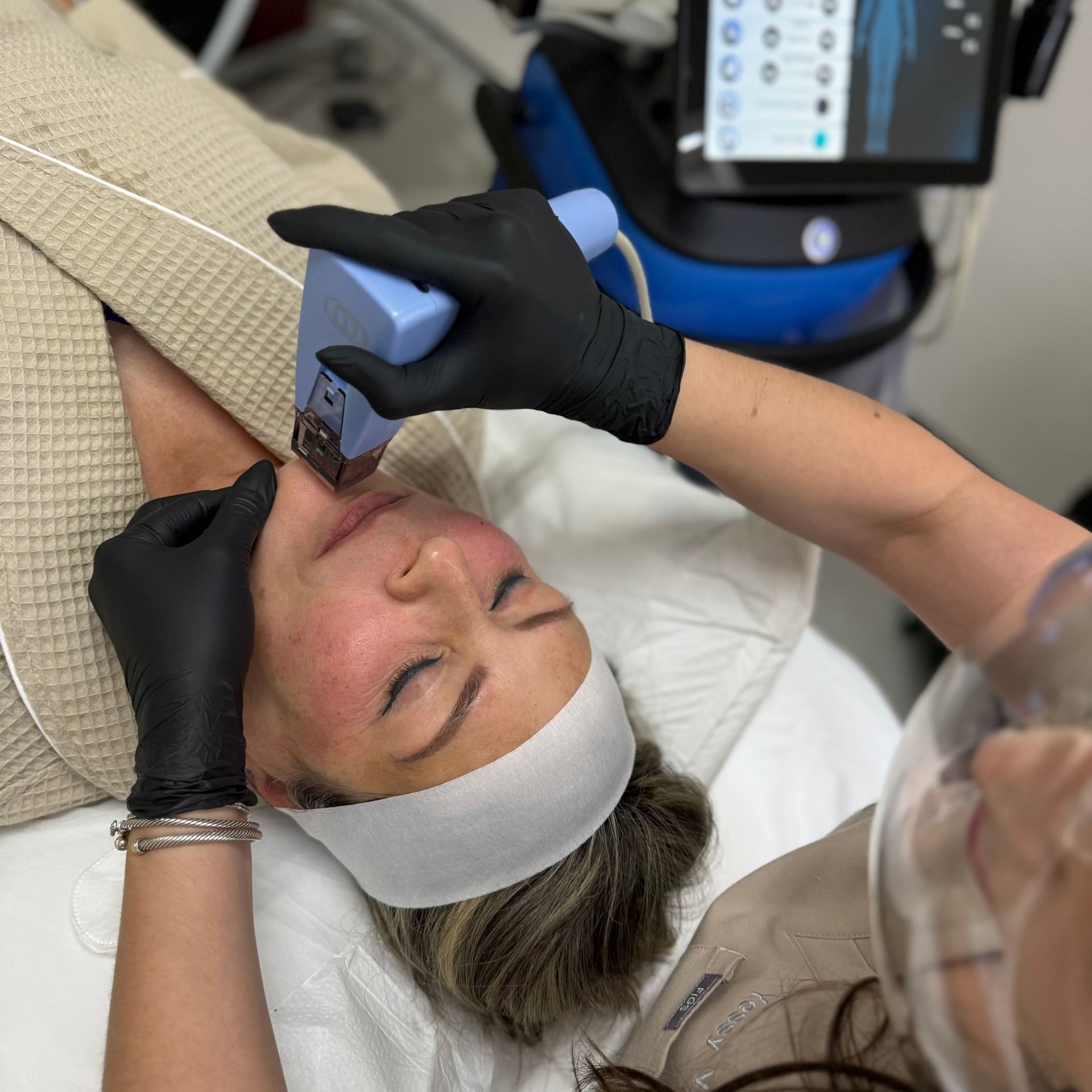 A provider in black gloves uses a handheld cosmetic laser device on a person’s jawline during a clinical skin treatment.
