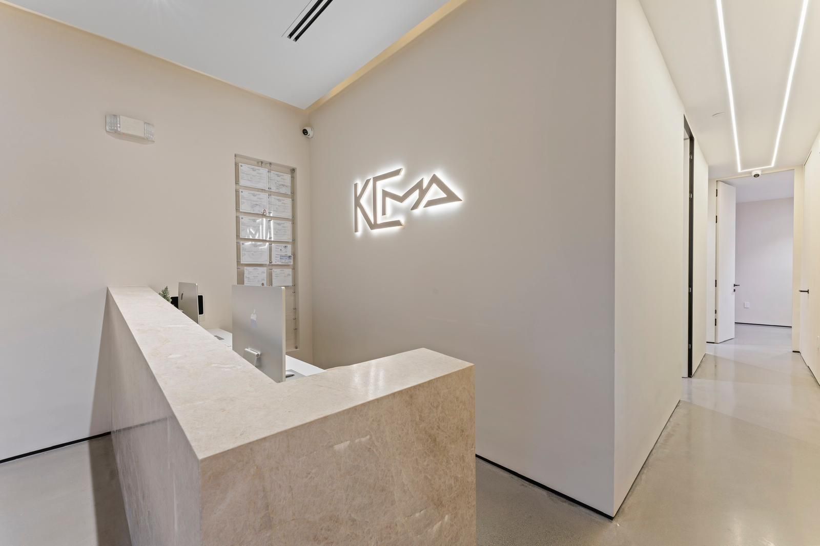 A minimalist reception area with a light-colored marble desk and a glowing white neon company sign on a beige wall.