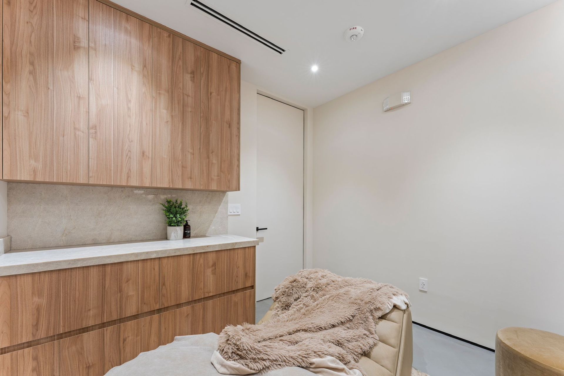 A modern room featuring light wood cabinets above a stone countertop, with a textured throw blanket on a seat.