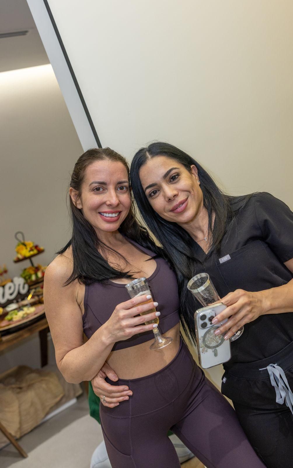 Two people smiling while holding glasses of champagne at a casual indoor gathering.