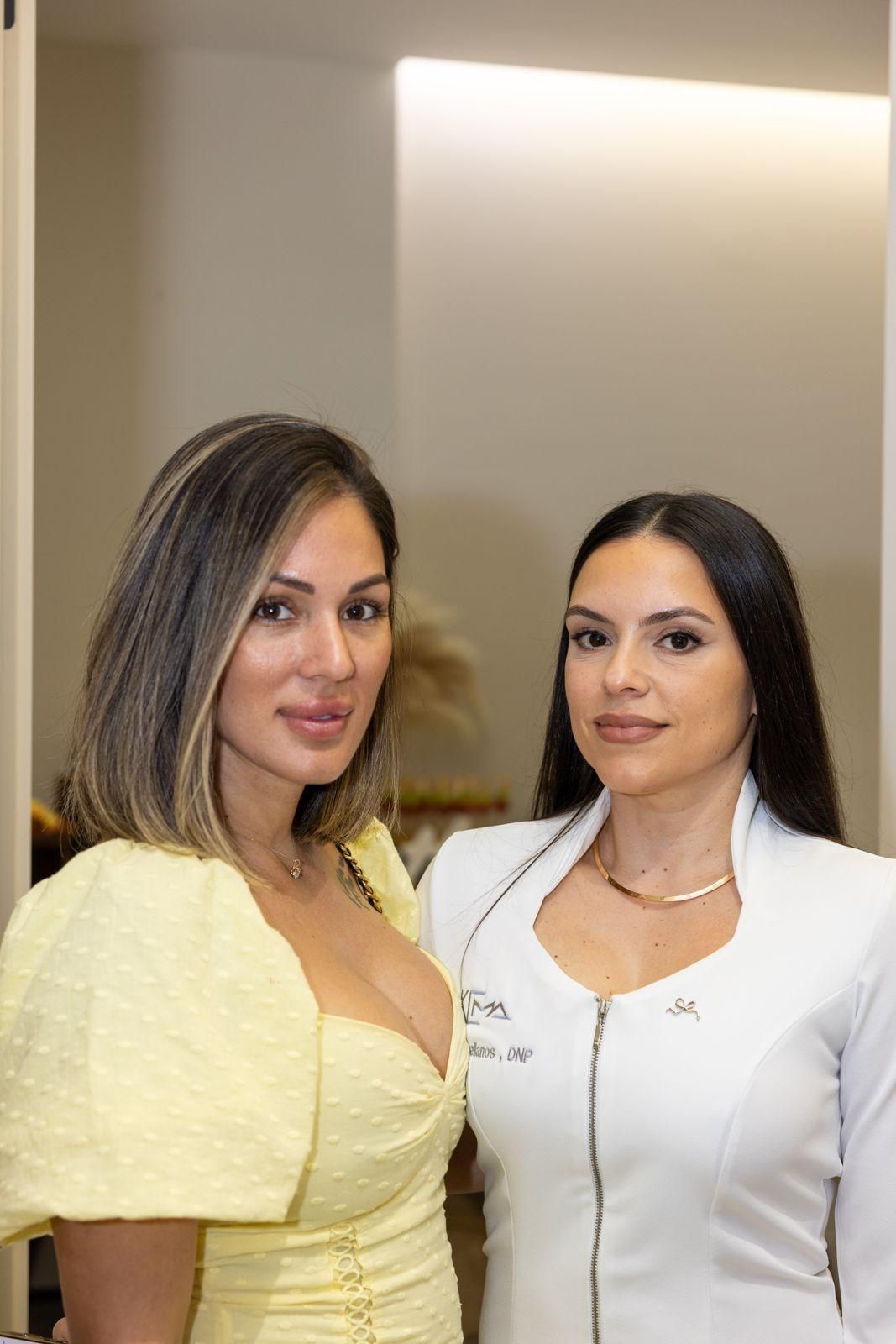 Two people standing side-by-side, one in a light yellow puff-sleeve top and the other in a white zipped uniform top.
